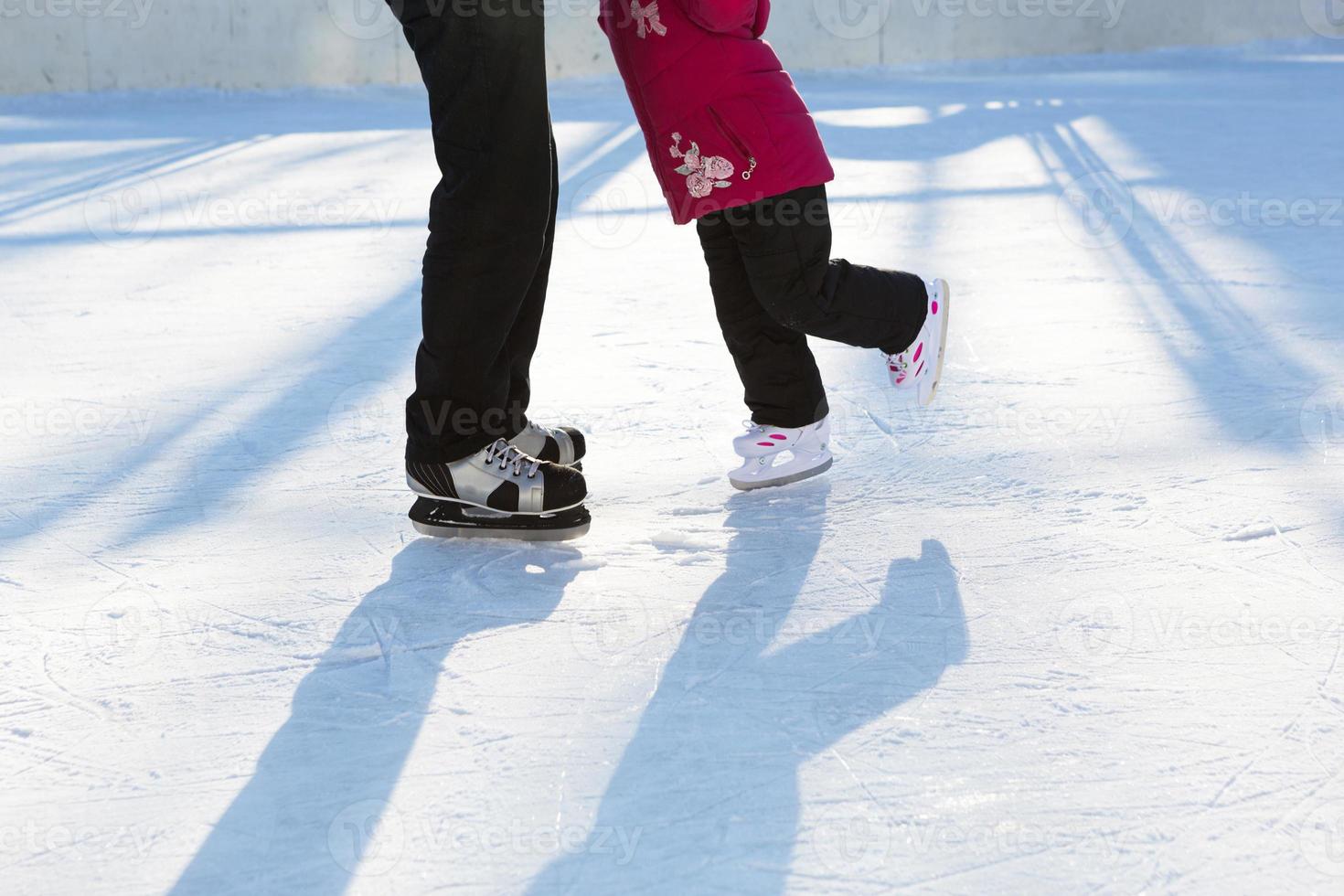 papá le enseña a su pequeña hija a patinar sobre hielo en una pista de patinaje en el patio de edificios de varios pisos en la ciudad. día soleado de invierno helado, deportes de invierno activos y estilo de vida foto