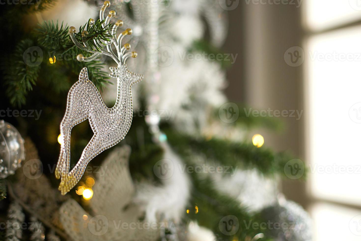 colgante de ciervo de cristal transparente en el árbol de navidad con guirnaldas de luces. decoración navideña blanca, plumas, globos, flores, cintas. año nuevo, el ambiente de celebración y magia. espacio para texto foto