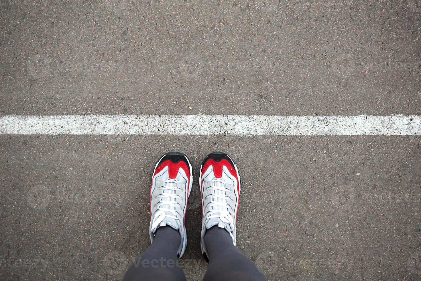 Feet in sneakers stand near the dividing line on the asphalt. Bounding line, social distance, waiting in line. The border, stand in line for a start. Copy space photo