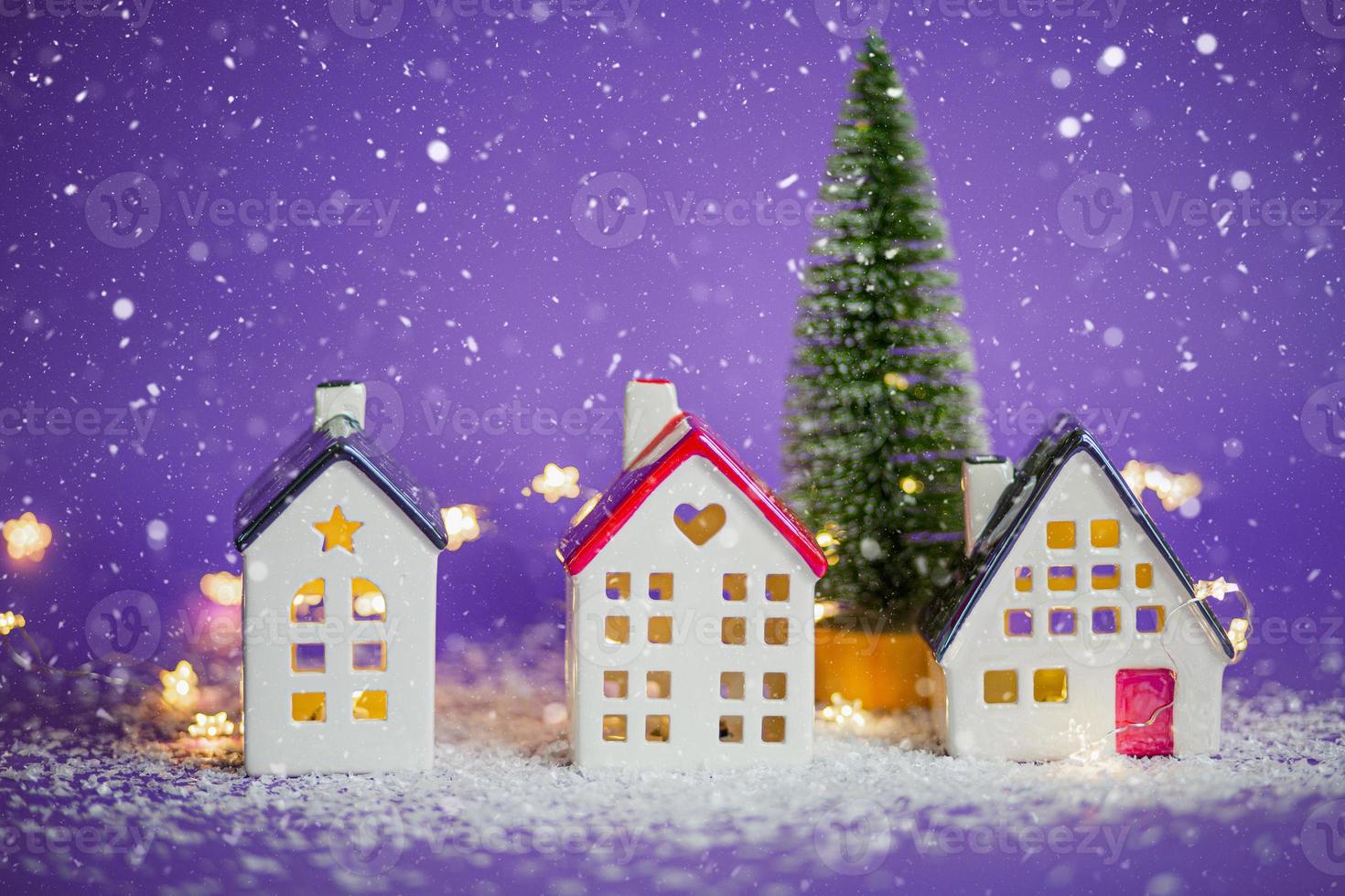 casas acogedoras y árbol de navidad en tormenta de nieve sobre fondo  violeta y luces de