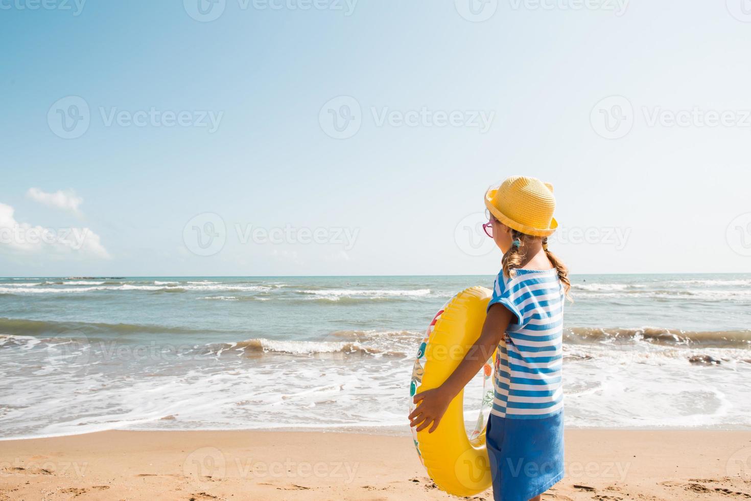 una niña con un círculo inflable amarillo en la orilla del mar. relajarse en la playa, viajes de verano. foto