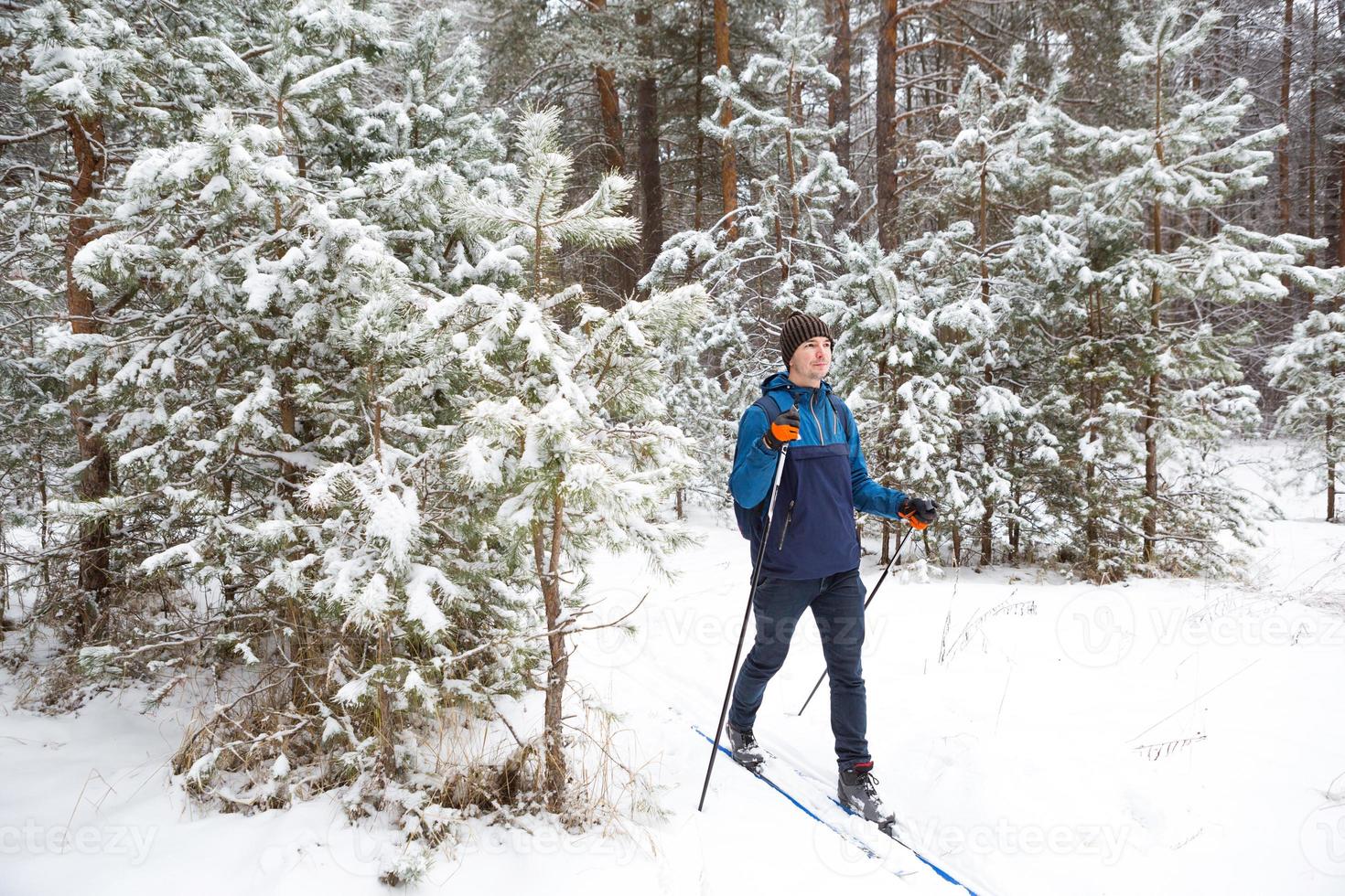 esquiador con mochila y sombrero con pompón con bastones de esquí en las manos sobre el fondo de un bosque nevado. esquí de fondo en bosque de invierno, deportes al aire libre, estilo de vida saludable, turismo de deportes de invierno. foto