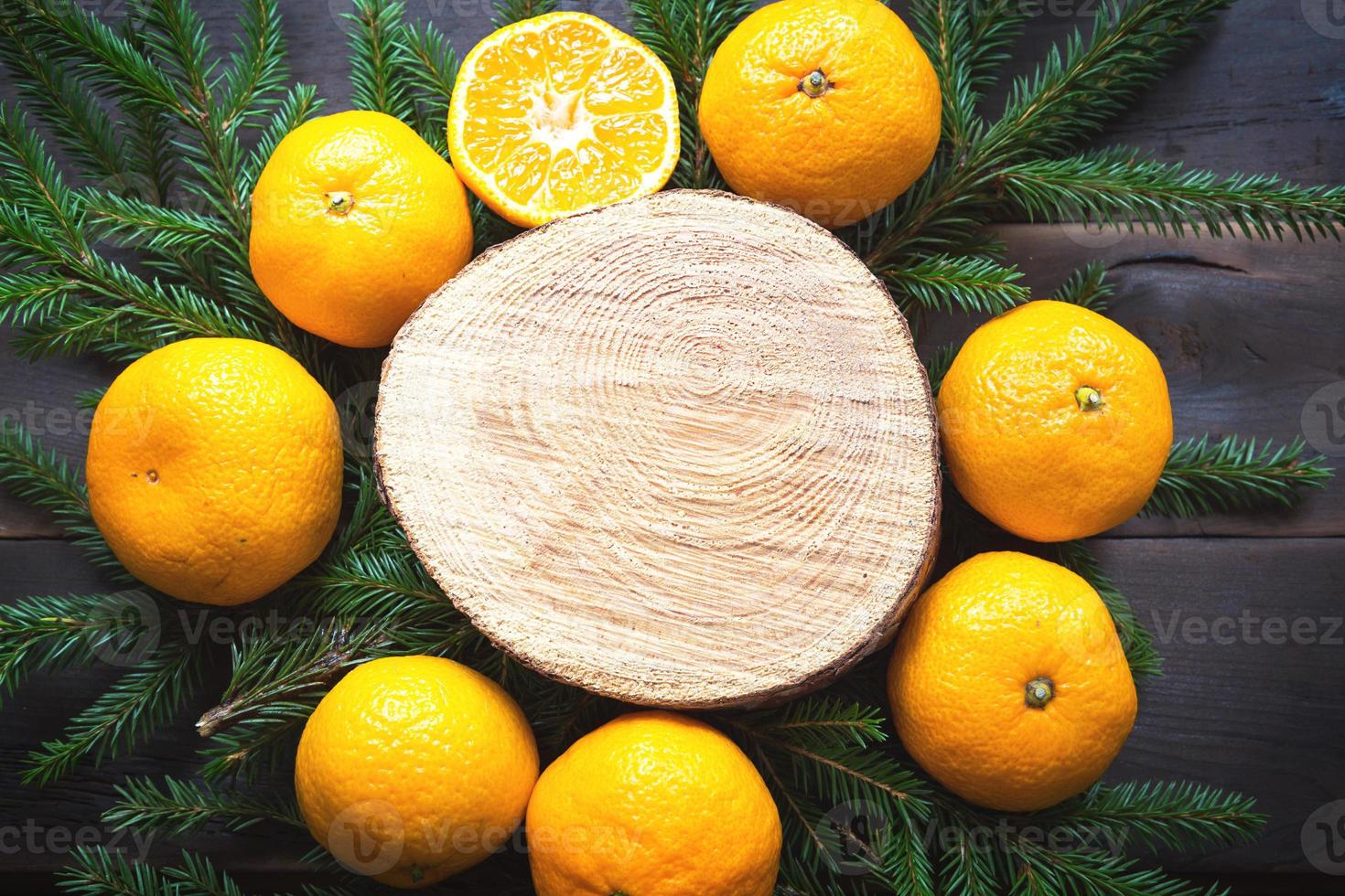 New year's holiday background on round cut of tree surrounded by tangerines, live fir branches and golden lights garlands, with wooden space for text. Citrus aroma, slices of orange, Christmas. frame photo