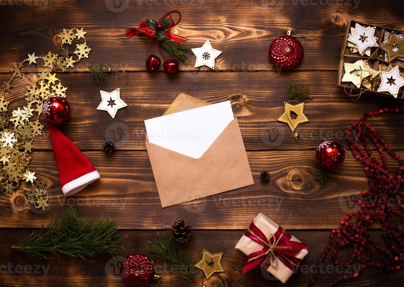 Mail envelope made of craft paper with a white sheet for text on a wooden background with Christmas decor. A letter to Santa Claus, a wish list, a new year's dream, a gift. Flat lay, copy space photo