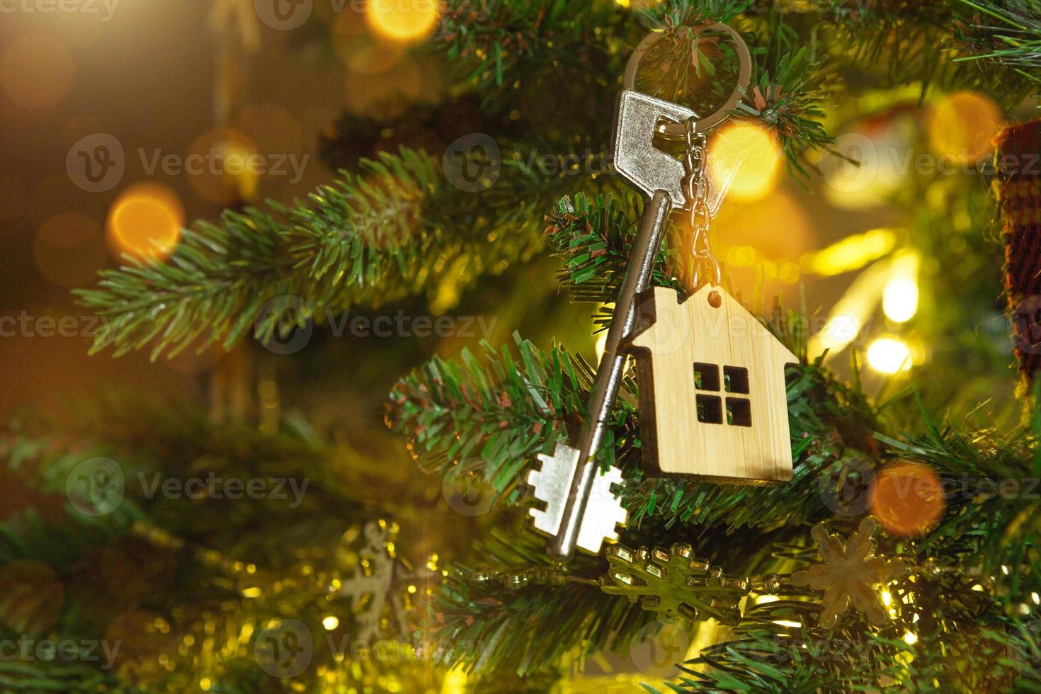 Key to the house with a keychain is hanging on the Christmas tree. A gift for New Year, Christmas. Building, design, project, moving to new house, mortgage, rent and purchase real estate. Copy space photo