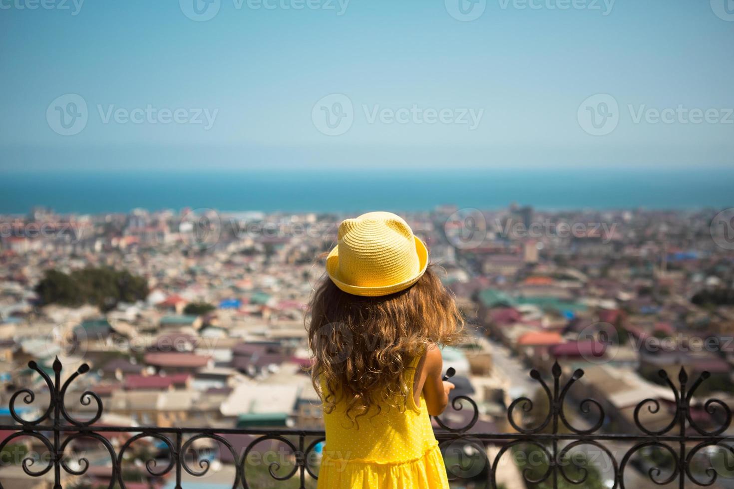 una chica turista con un sombrero amarillo y un vestido de verano mira desde una altura en la plataforma de observación de la ciudad. visita turística. el niño se perdió, buscando a los padres foto