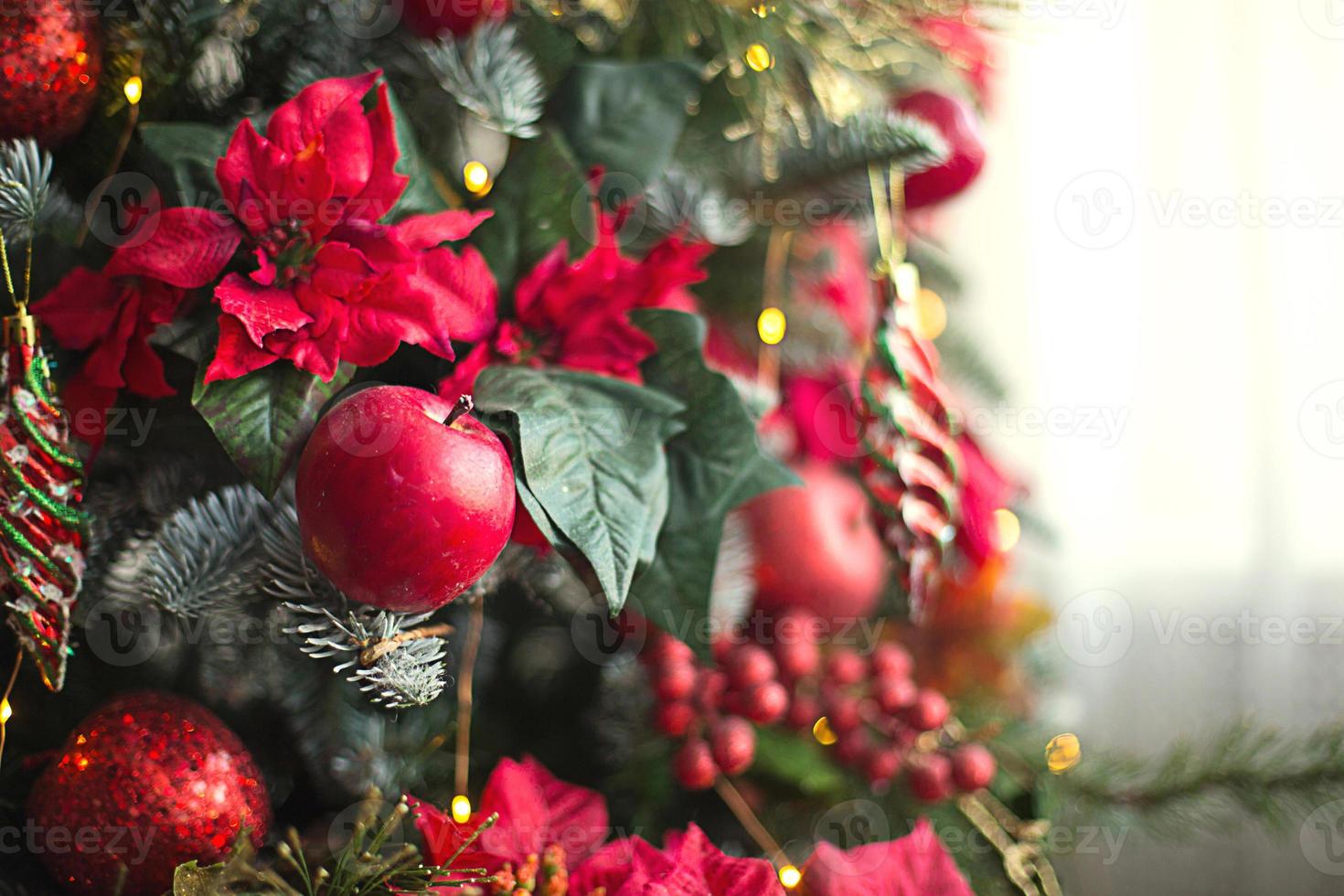 decoración roja en un árbol de navidad hecho de manzanas y poinsettias. fondo de navidad y marco para año nuevo. primer plano, abeto festivo con bayas, carámbanos, guirnaldas. espacio para texto foto