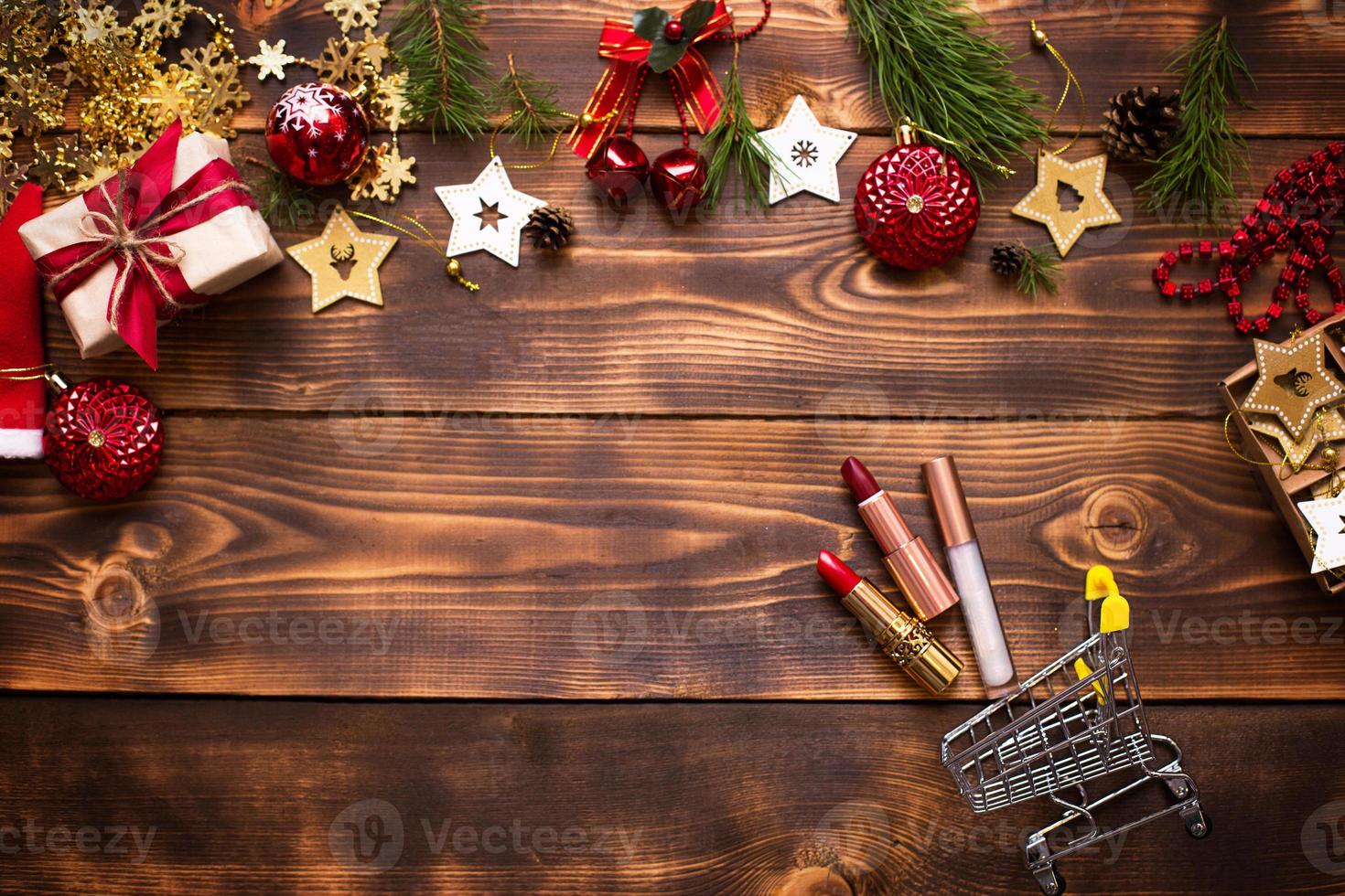 lápiz labial rojo y brillo de labios y párpados sobre un fondo de madera en un carrito de supermercado de metal en la decoración navideña. maquillaje de vacaciones para año nuevo, regalos, compras, deseos de mujeres. espacio para texto, plano foto