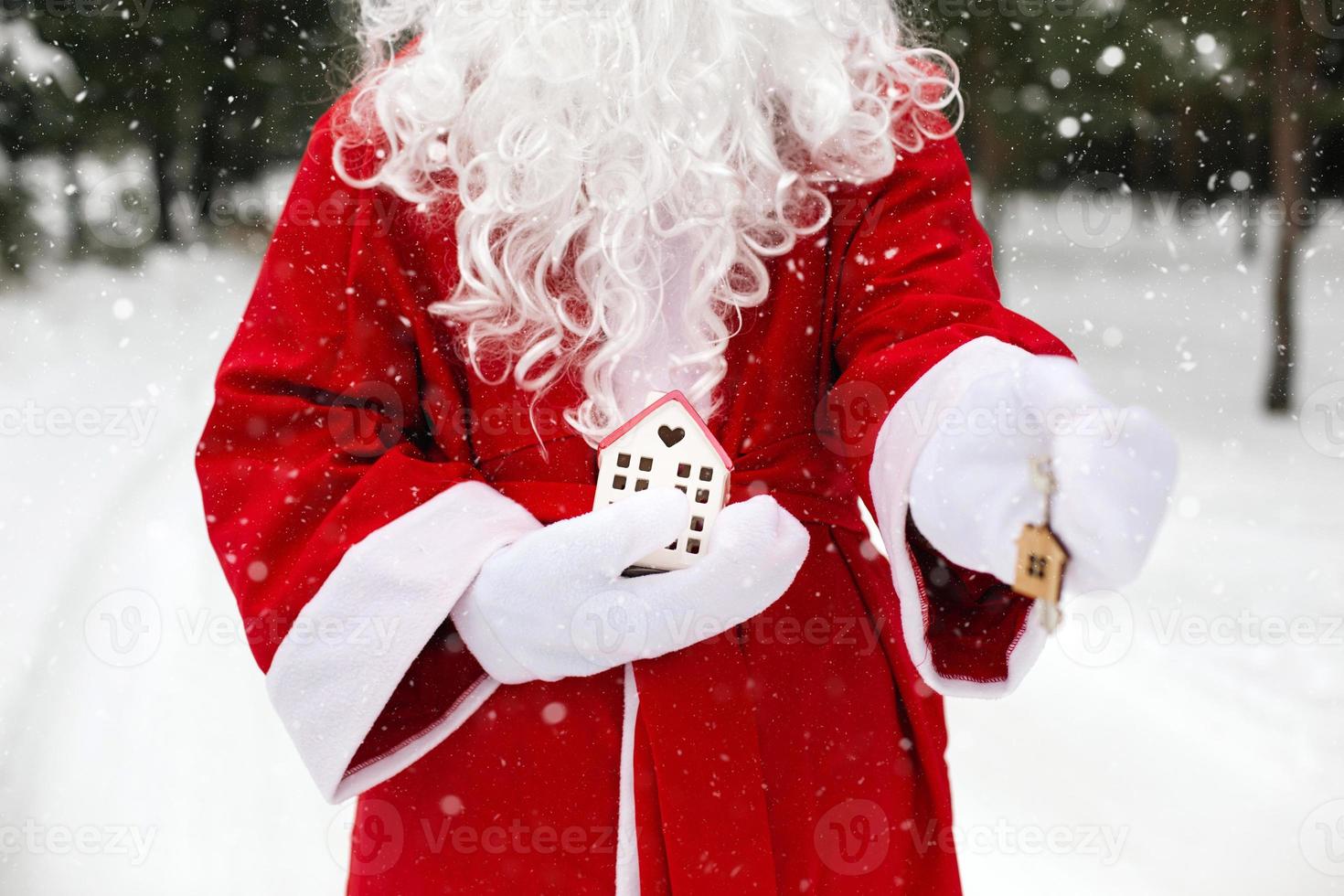 House key with keychain cottage in hands of Santa Claus outdoor in snow. Deal for real estate, purchase, construction, relocation, mortgage. Cozy home. Merry Christmas, new year booking event and hall photo