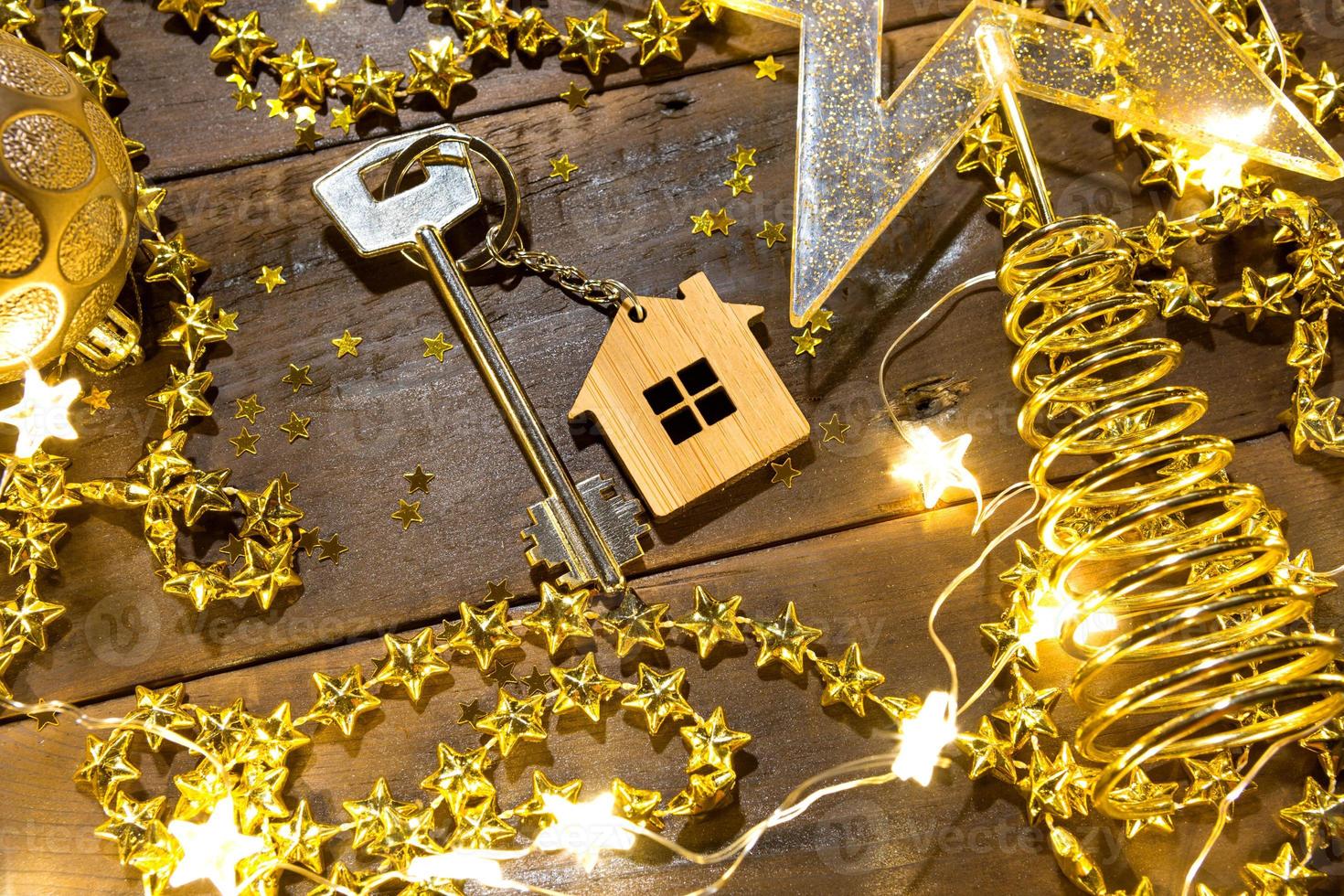 llave de la casa con cabaña de llavero sobre un fondo festivo con lentejuelas, estrellas, luces de guirnaldas. feliz año nuevo-letras de madera, saludos, tarjetas de felicitación. compra, construcción, reubicación, hipoteca foto