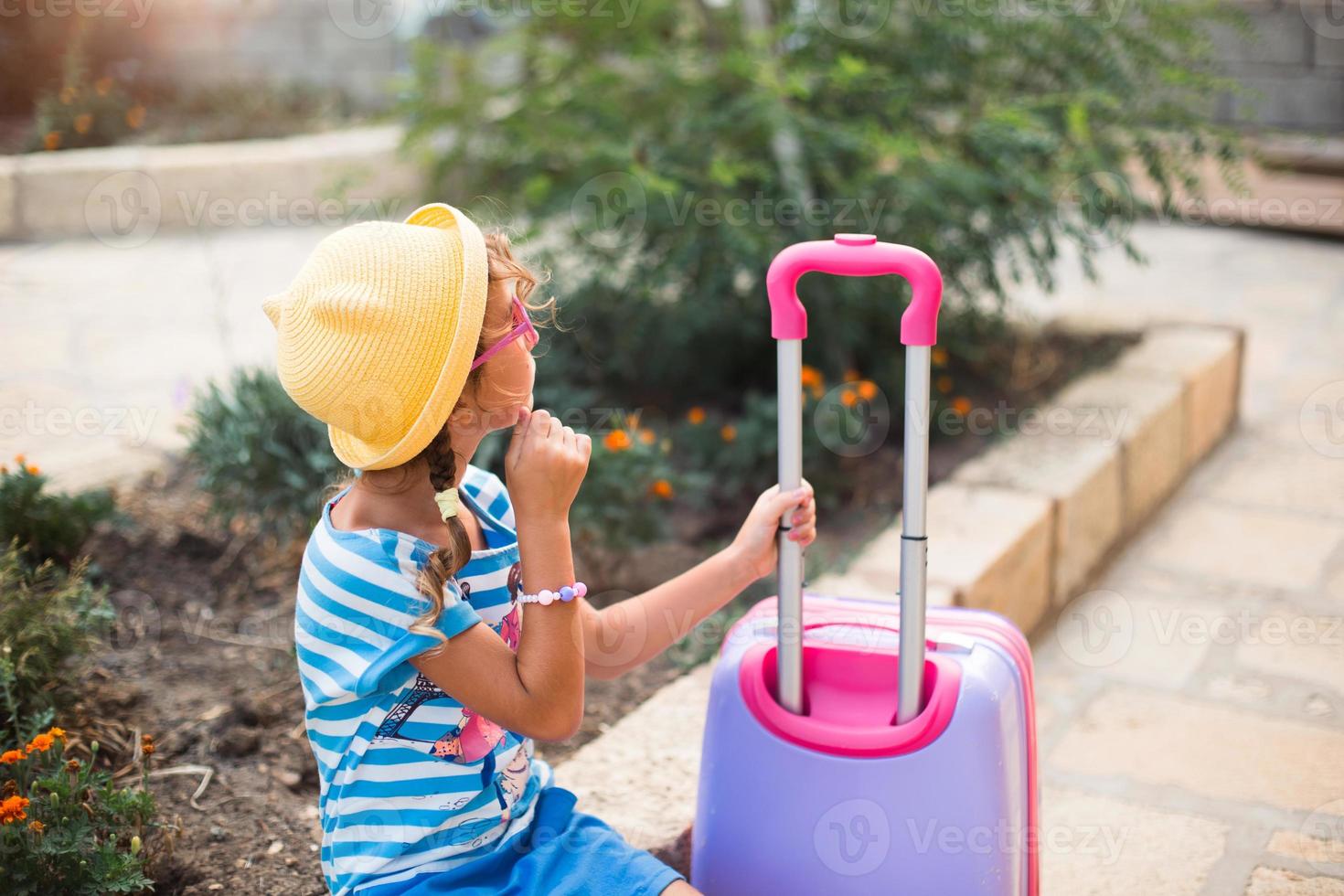 A girl with a suitcase, a hat and sunglasses is going on vacation. Waiting for the trip, arrival at the place of residence at the hotel. photo