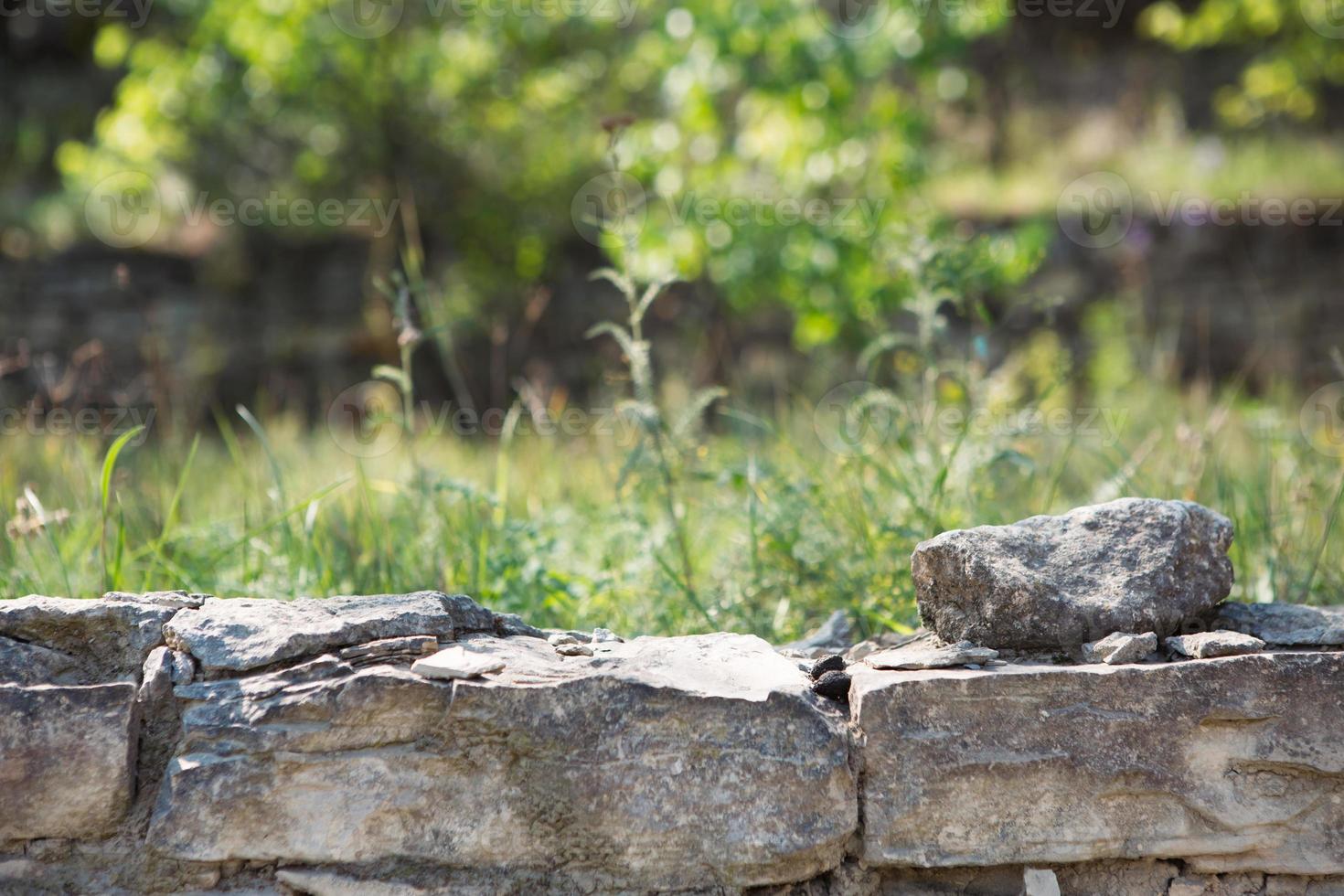 Masonry walls of natural sand color with green natural vegetation in the background in defocus.. Stone texture close-up foreground, ecology, eco-friendly theme photo