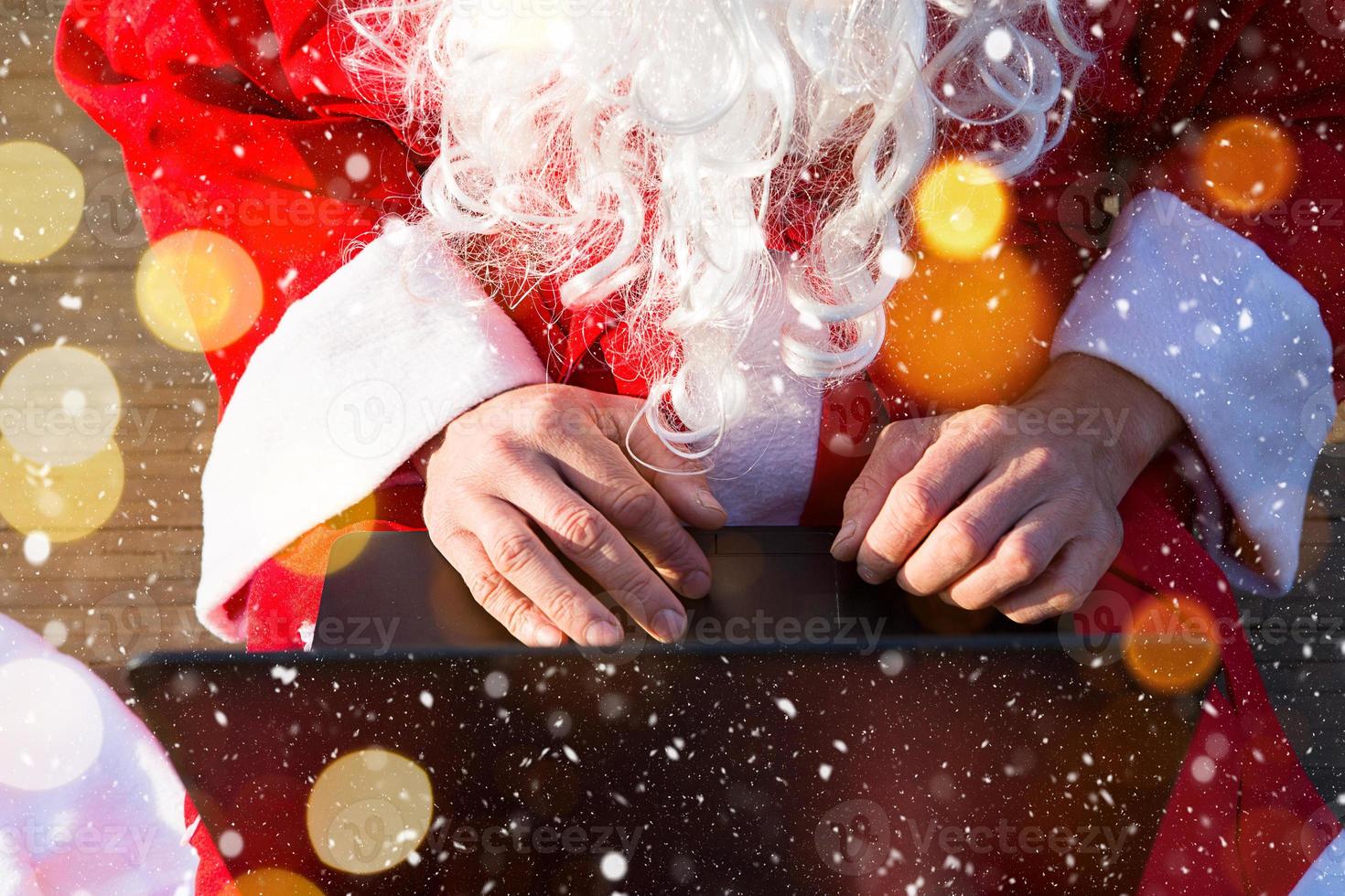 Santa Claus with a laptop and a gift in his hand. Order gifts for Christmas and new year through the online store. Booking the services of an animator for the holidays. photo