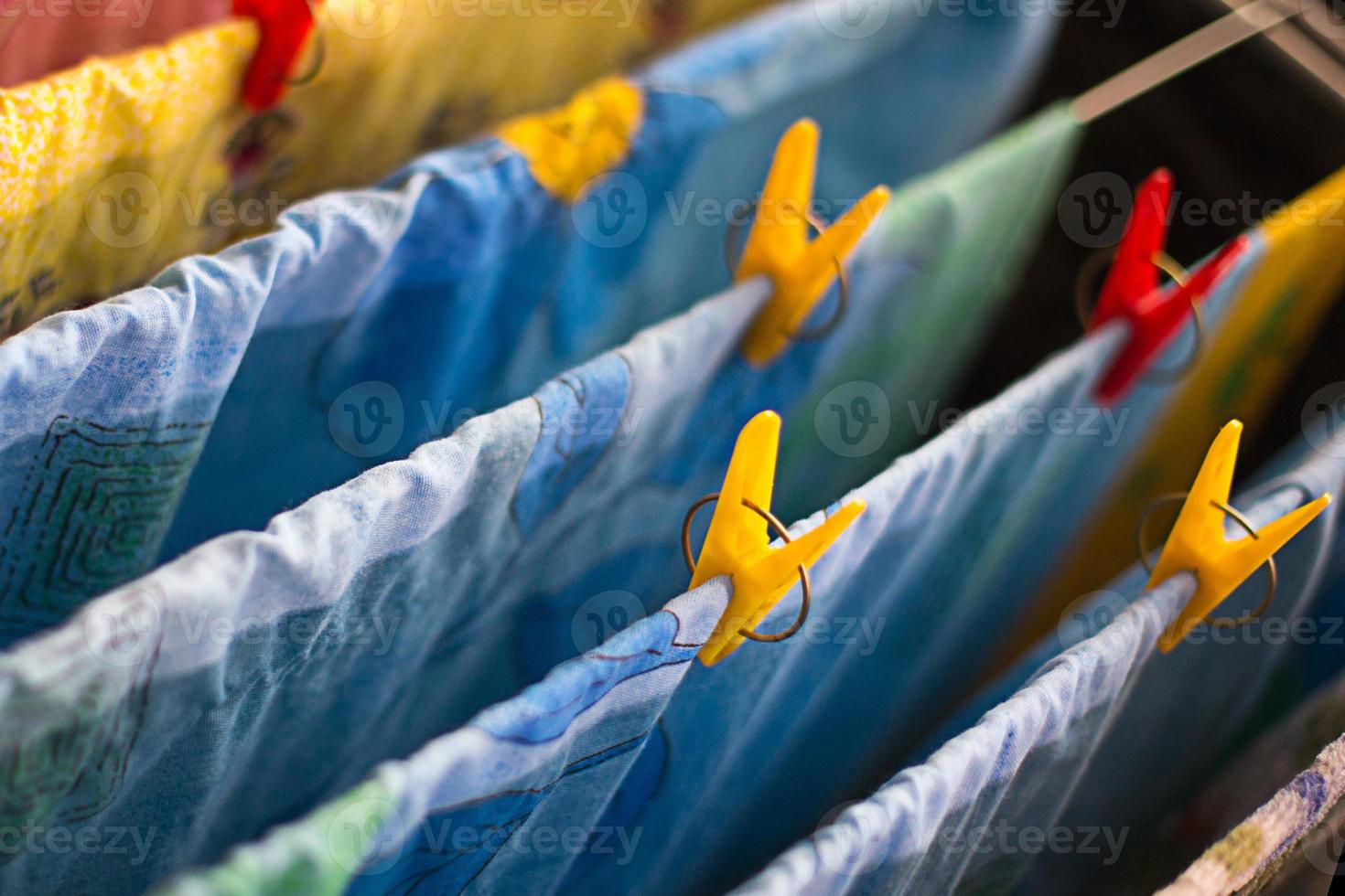 Colorful clean bed linen and towels after washing are hung on the bars of the dryer and secured with yellow and red clothespins. General cleaning, Laundry drying, compact dryer for the house. photo