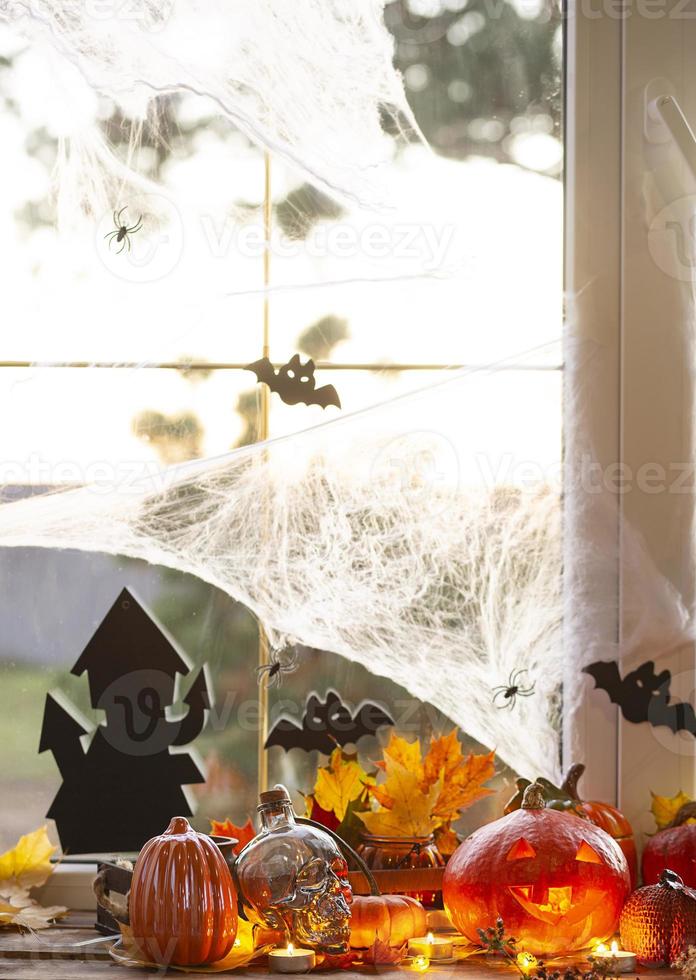 Festive decor of the house on the windowsill for Halloween - pumpkins, Jack o lanterns, skulls, bats, cobwebs, spiders, candles and a garland - a cozy and terrible atmosphere photo