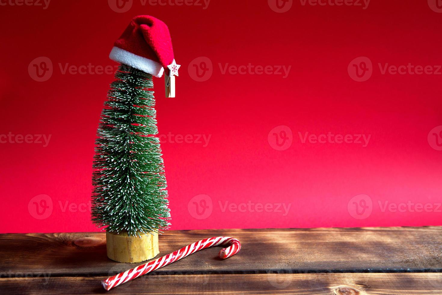 árbol de navidad sobre un fondo rojo con luces de guirnaldas, bastón rayado de caramelo, sombrero de santa, oropel. año nuevo, ambiente festivo. copie el espacio foto