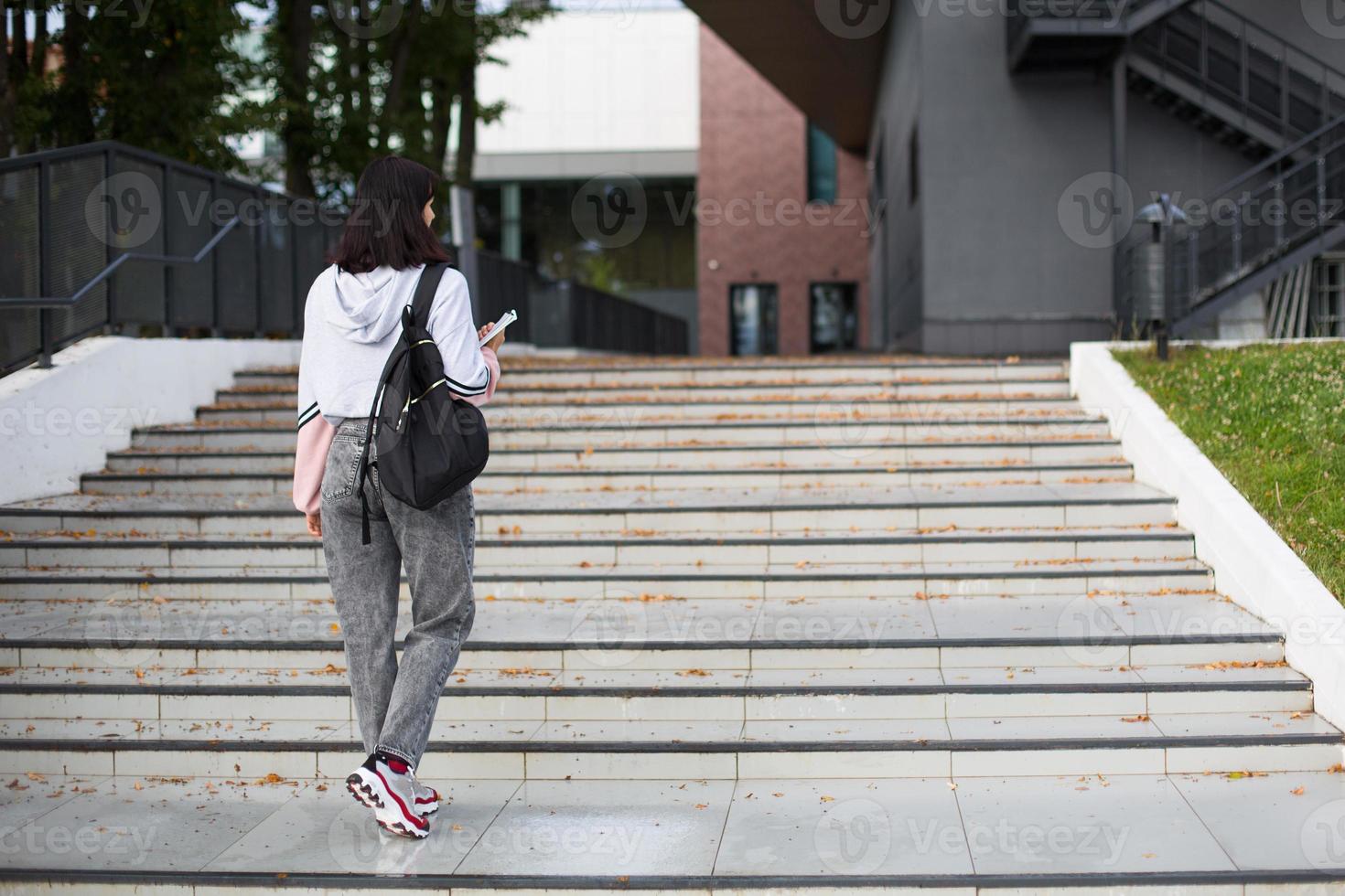 A female student with a black backpack and a notebook in her hands stands on the steps in front of the Institute. Higher education, the beginning of the school year, back to school. Copyspace photo