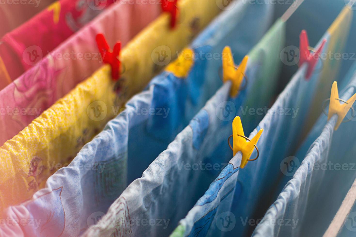 La ropa de cama y las toallas limpias y coloridas después del lavado se cuelgan en las barras de la secadora y se aseguran con pinzas de ropa amarillas y rojas. limpieza general, secado de ropa, secadora compacta para la casa. foto