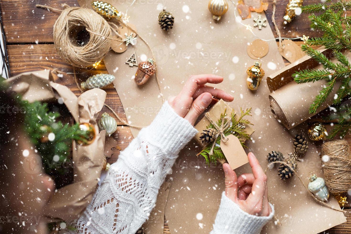 Hands pack a gift for Christmas and new year in eco-friendly materials kraft paper, live fir branches, cones, twine, tied with a bow. Tags with mock up, natural decor, hand made, flatly. Festive mood photo