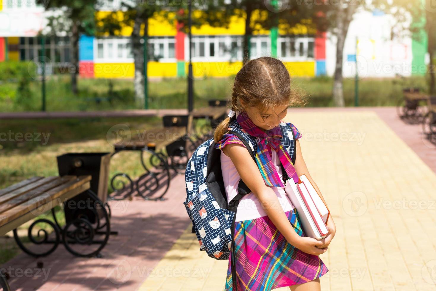 Girl with a backpack and a stack of books near the school. Back to school, the child is tired, heavy textbooks. Education, primary school classes, the beginning of the school year, September 1 photo