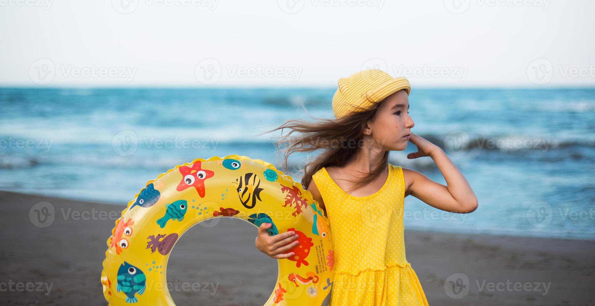 una niña con un círculo inflable amarillo en la orilla del mar. relajarse en la playa, viajes de verano. foto