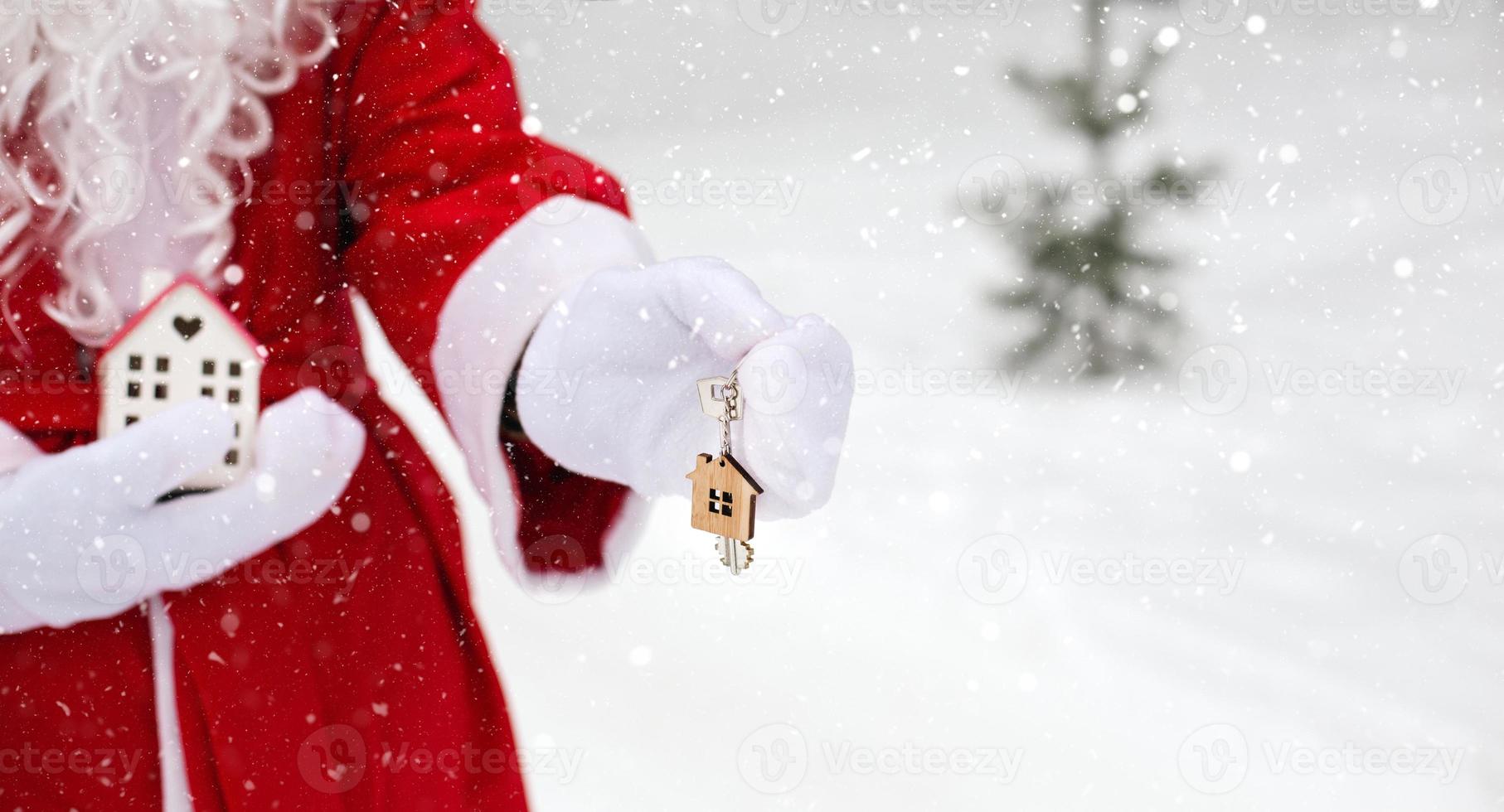House key with keychain cottage in hands of Santa Claus outdoor in snow. Deal for real estate, purchase, construction, relocation, mortgage. Cozy home. Merry Christmas, new year booking event and hall photo
