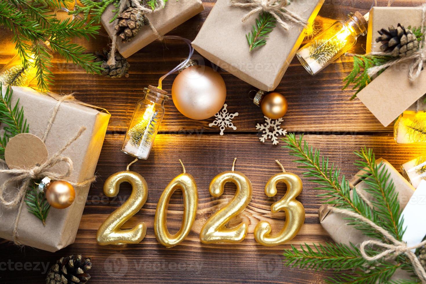 Figures candles 2023 on a wooden background with fairy lights, gifts box and eco-friendly Christmas decor. Tags with mock up, natural decor, cones, needles. Festive mood. Flatly, new year background photo