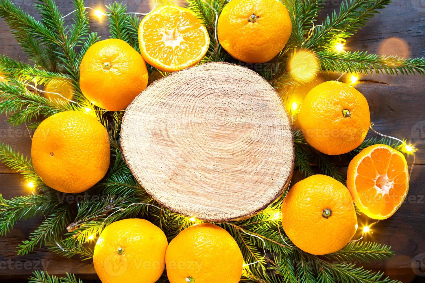 New year's holiday background on round cut of tree surrounded by tangerines, live fir branches and golden lights garlands, with wooden space for text. Citrus aroma, slices of orange, Christmas. frame photo