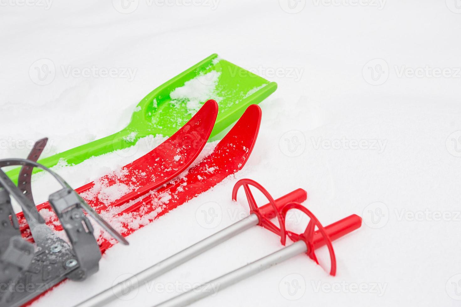 Children's red skis with sticks and a green snow shovel -layout in the snow. Winter outdoor activities, family fun. White natural frosty background. Copy space photo