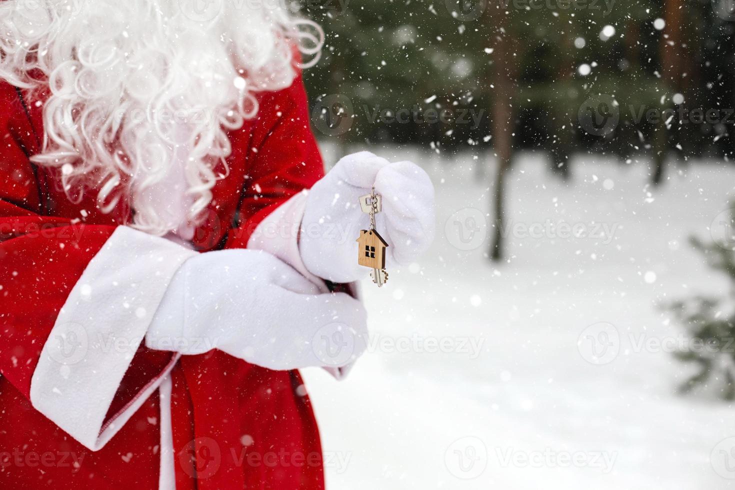 House key with keychain cottage in hands of Santa Claus outdoor in snow. Deal for real estate, purchase, construction, relocation, mortgage. Cozy home. Merry Christmas, new year booking event and hall photo