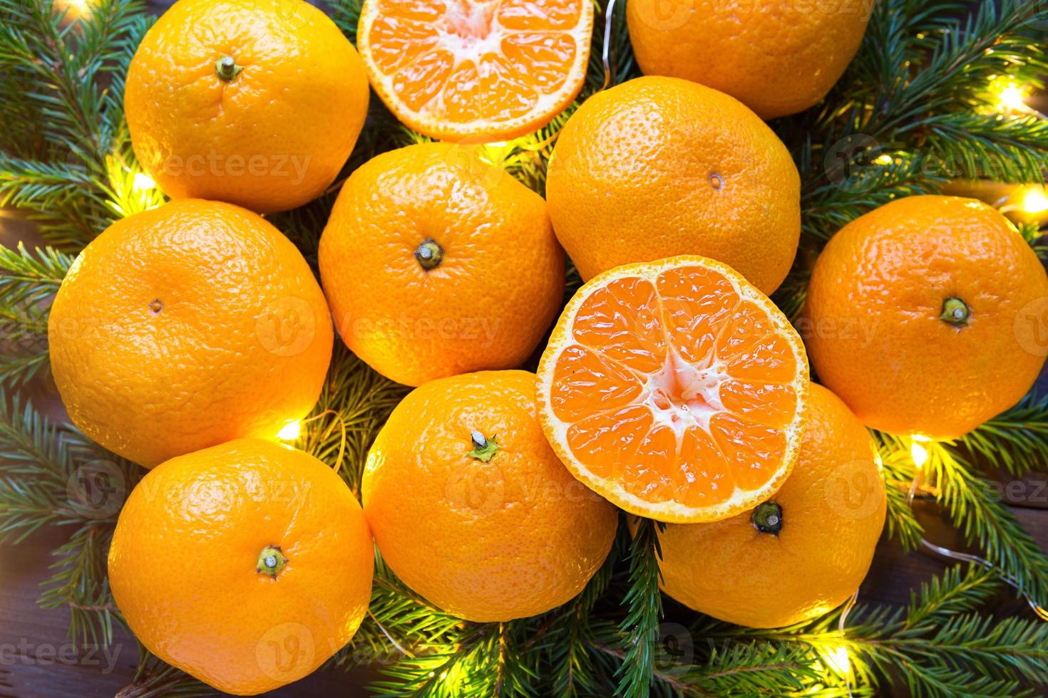 mandarinas frescas en luces de guirnaldas, en ramas de abeto y oropel - fondo brillante de año nuevo. la mitad de una naranja, aroma cítrico de la fiesta. navidad, año nuevo. espacio para texto. foto