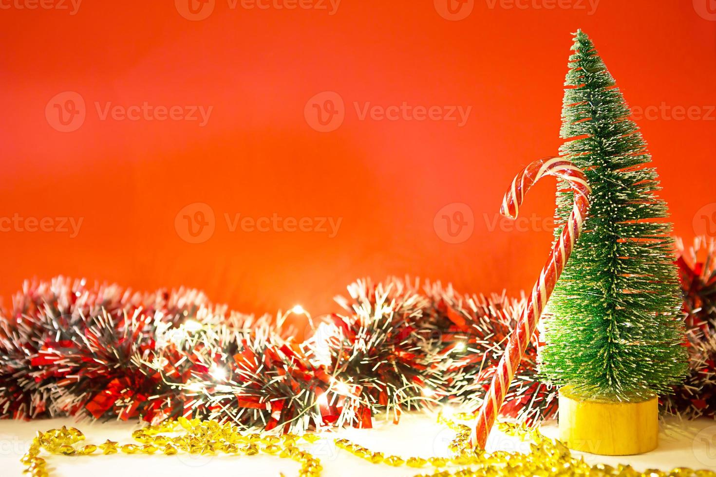 árbol de navidad sobre un fondo rojo con luces de guirnaldas, bastón rayado de caramelo, sombrero de santa, oropel. año nuevo, ambiente festivo. copie el espacio foto