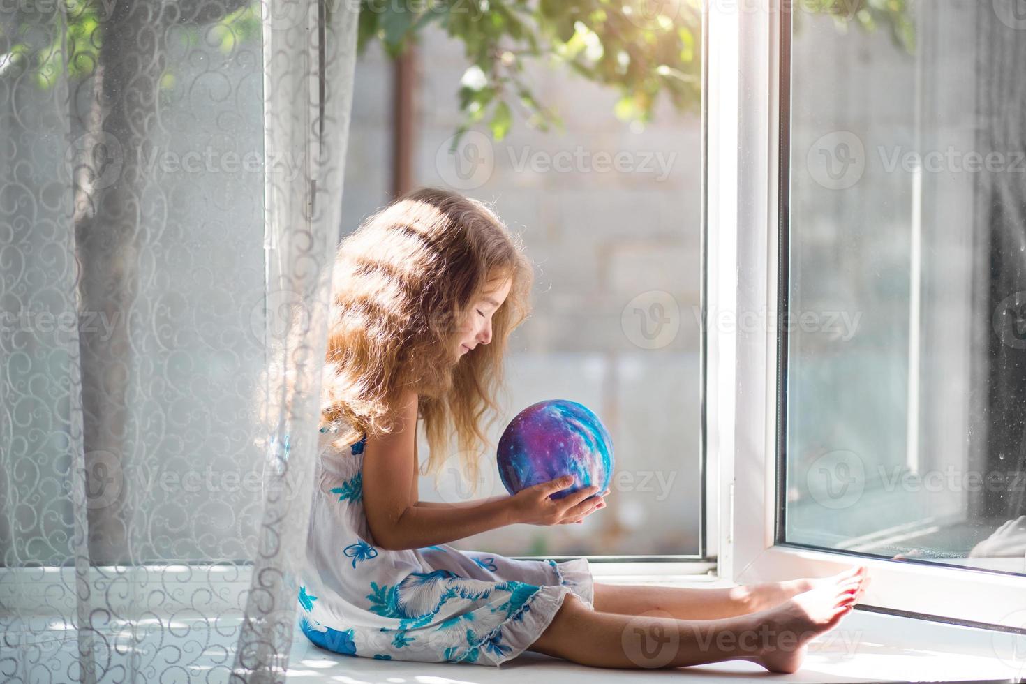 la niña en la ventana de la casa sostiene una lámpara en forma de planeta, un globo. paz, ecología, medio ambiente, pacífico foto