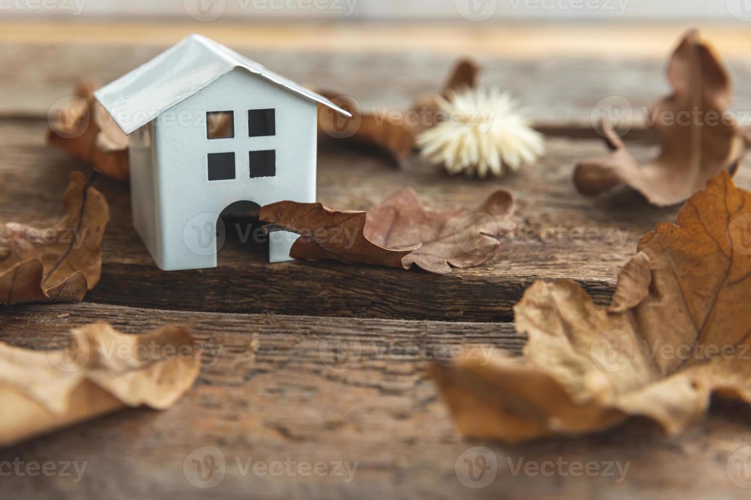 Autumnal Background. Toy house and dried fall leaves on wooden background. Thanksgiving banner copy space. Hygge mood cold weather concept. Hello Autumn with family. photo