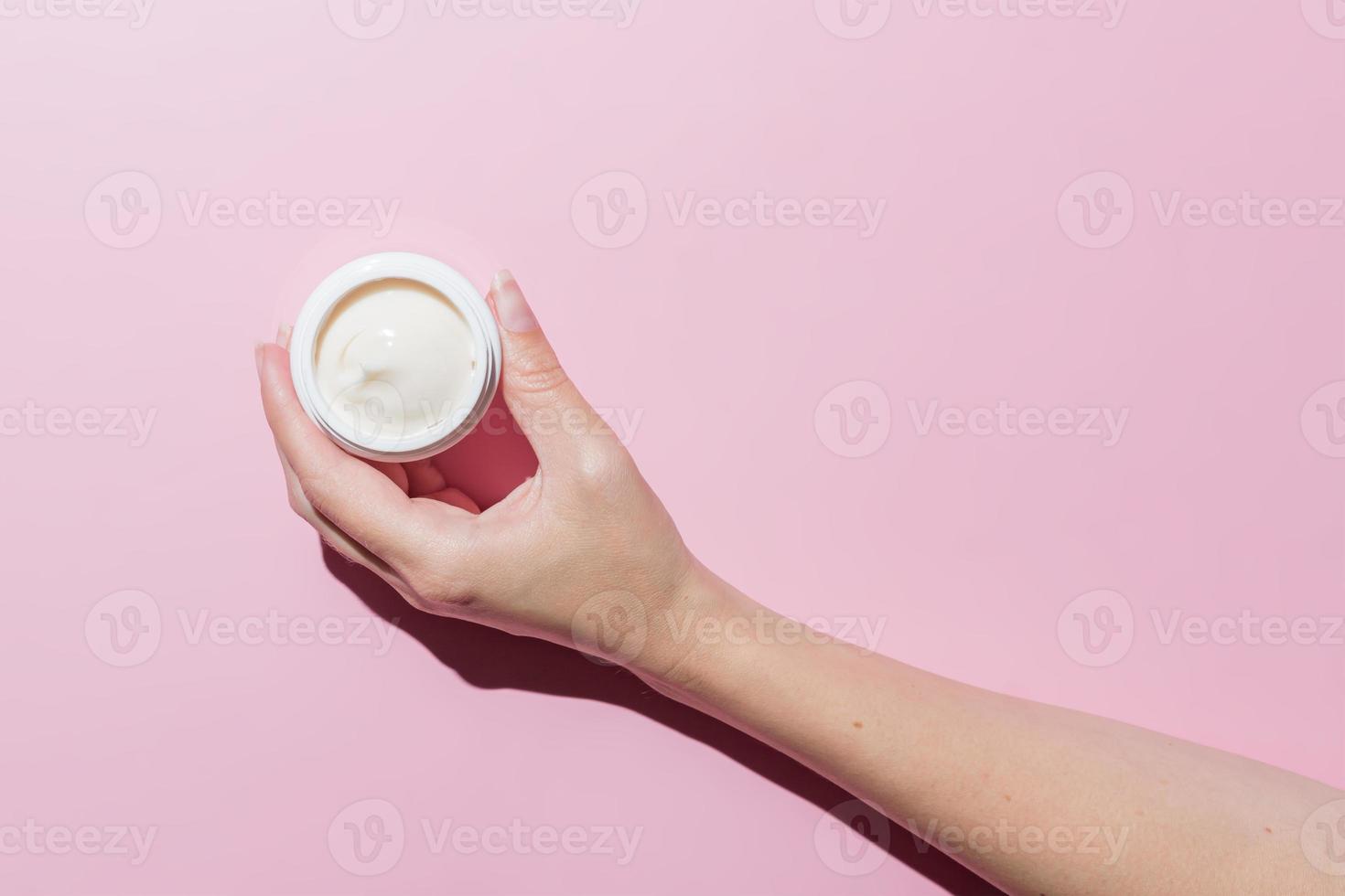 Woman Hand holding an open cosmetic cream container on pink background. Mockup with space for text. Branding presentation of cosmetic product photo