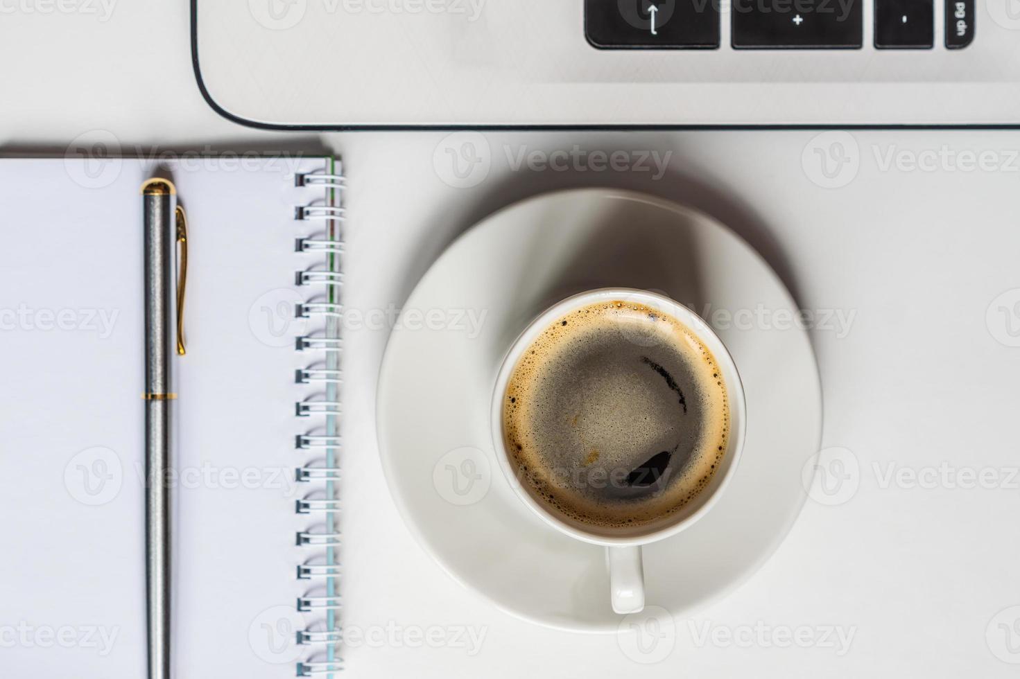 top view of white office desk with white laptop, notebook, metallic pen and cup of black coffee. Business concept photo