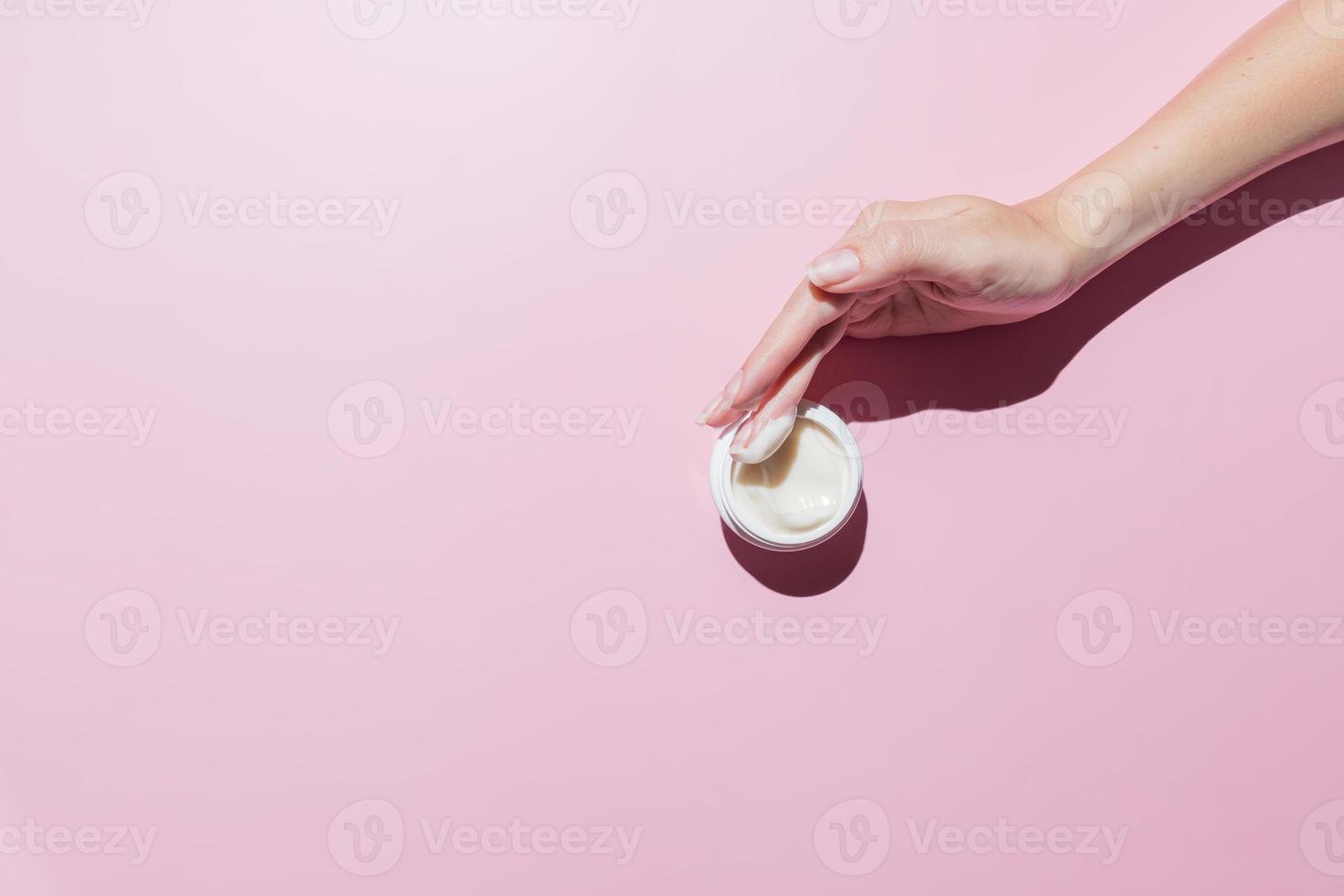 Woman hand with a cream on on a pink background. Groomed hands, natural short nails, m.ockup cosmetics photo