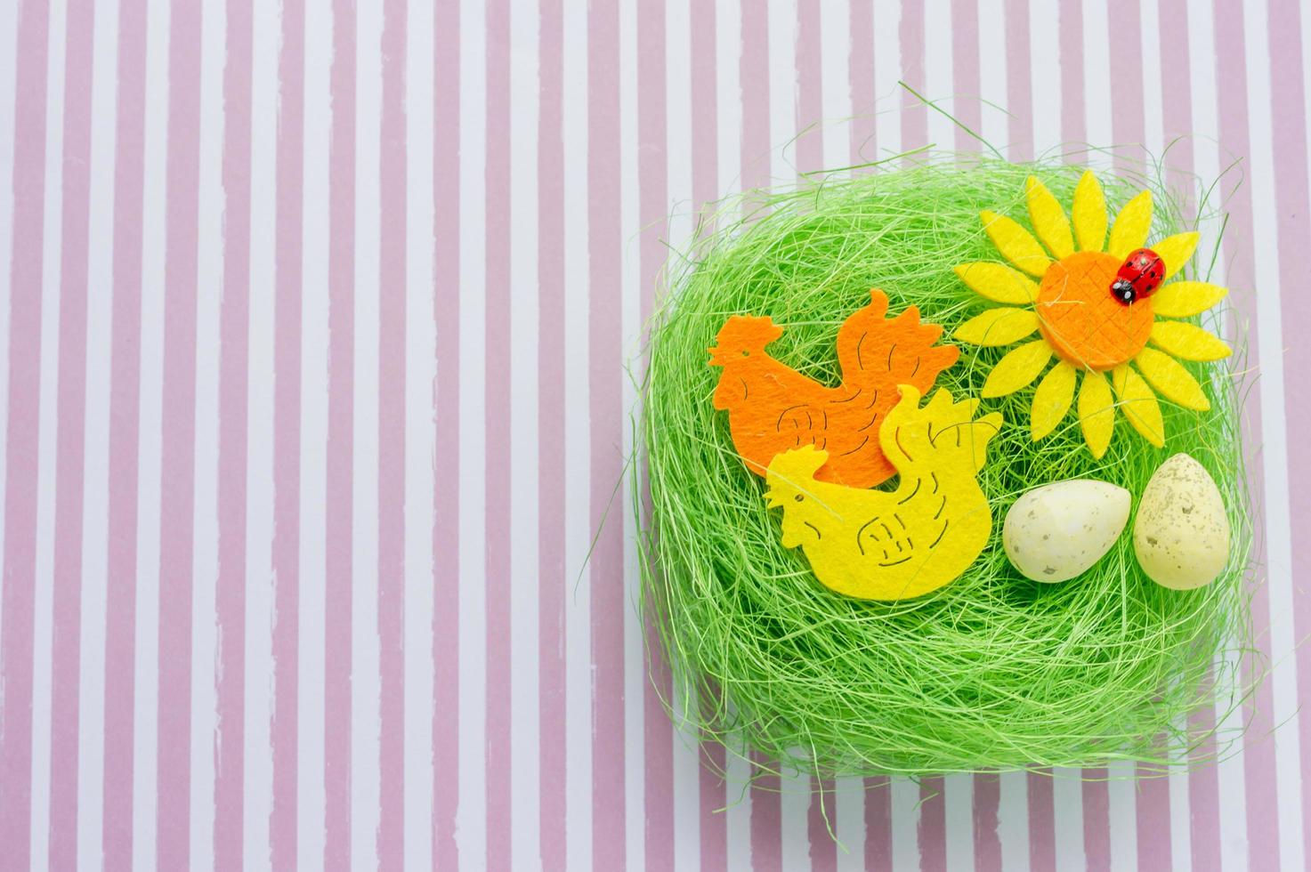 Green artificial nest with two colored cocks, egg and sunflower on striped background photo