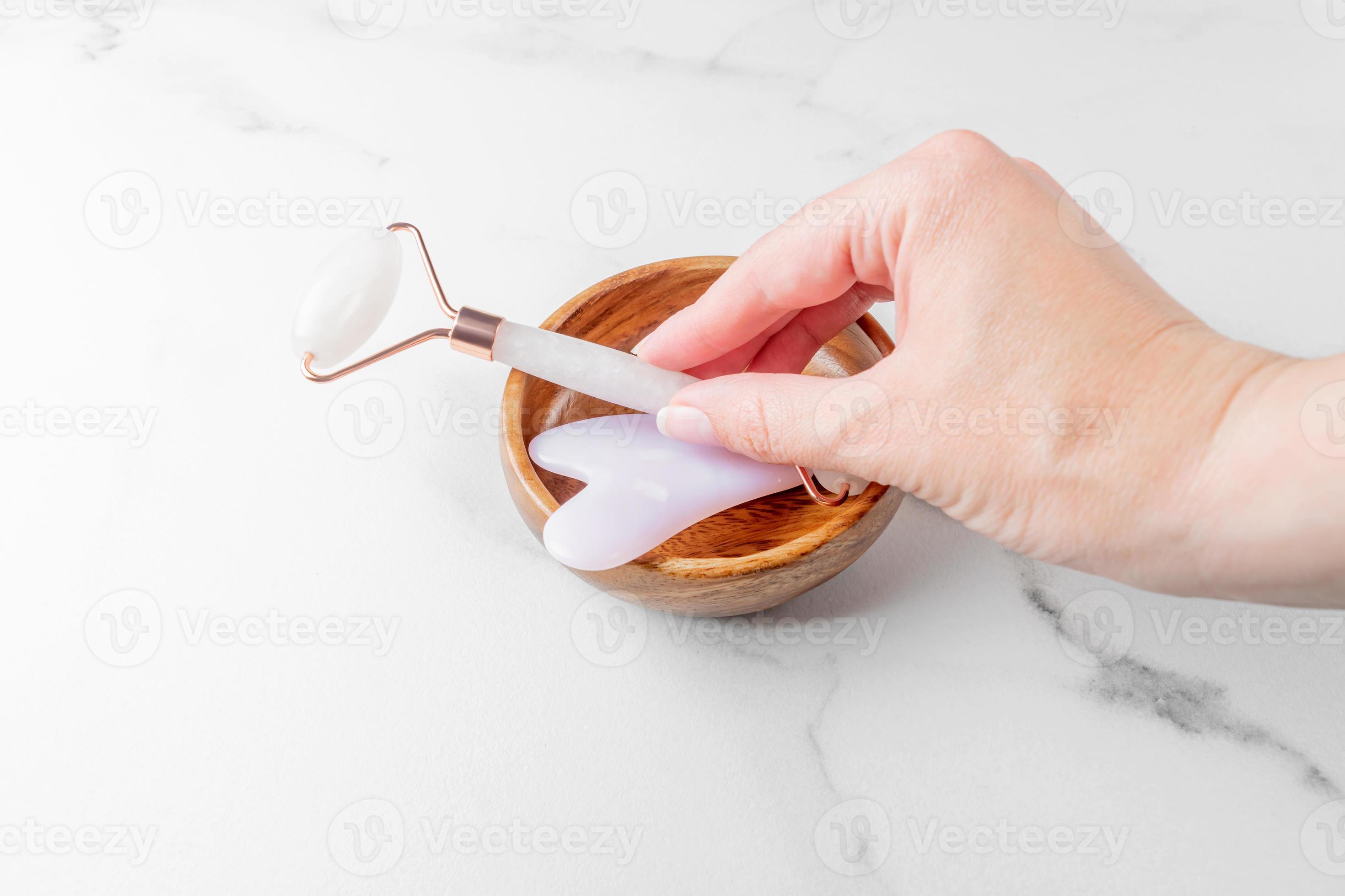 Female hand taking quartz stone massage roller. Rose quartz jade roller