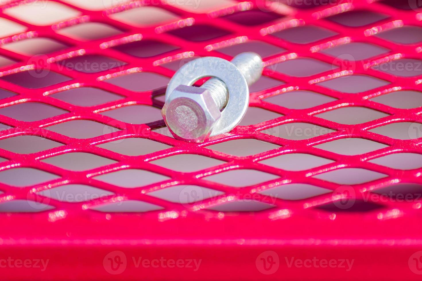 screw and nut lying on red metal grill, closeup photo