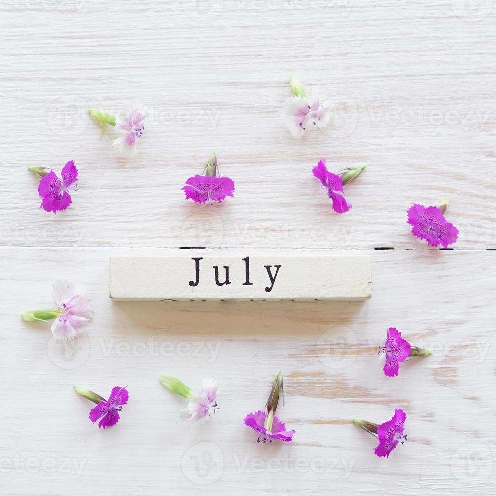 top view of wooden calendar with July sighn and pink flowers. photo