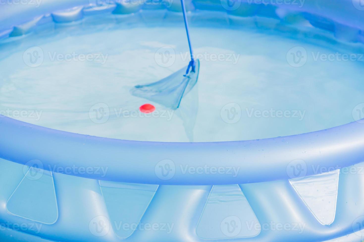 cleaning of garden swimming pool . Boy tries to cach red ball with Skimmer net photo