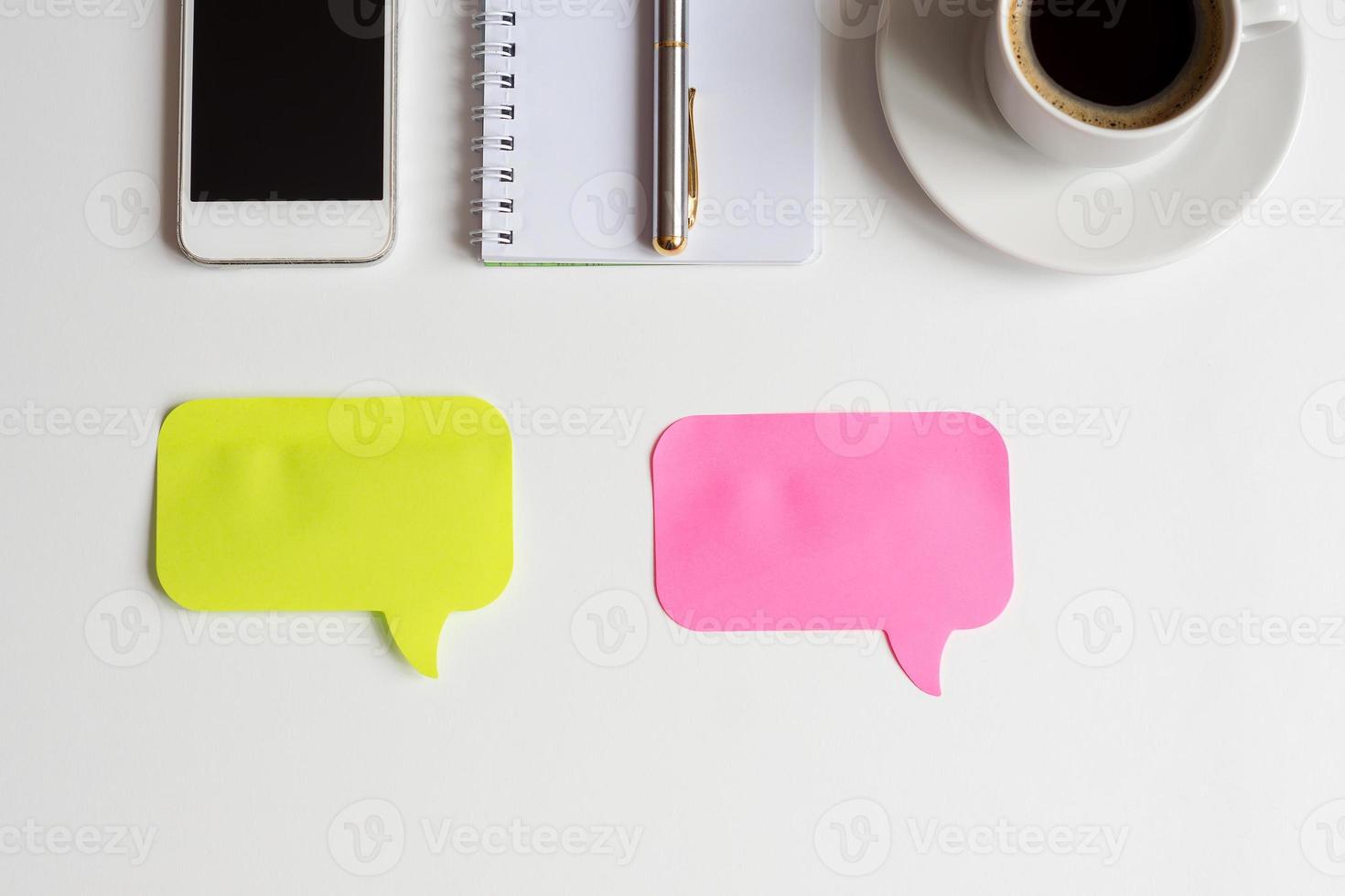 top view of white office desk, two colored stickers for notes, smartphone, notebook with metallic pen and cup of black coffee, business mockup photo