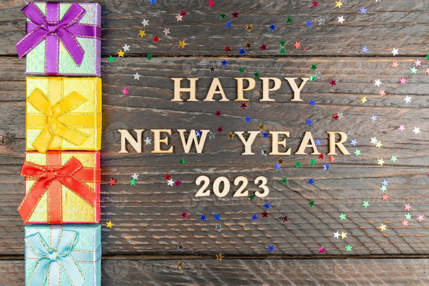 Multicolored gift boxes. New year presents on wooden table. Tex Happy new year 2023. Festive greeting card. Flat lay. photo