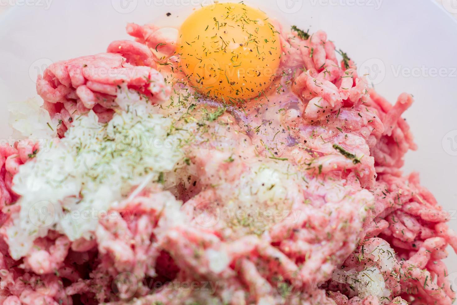 Minced meat in a bowl with raw egg, spices and chopped onion for cooking cutlets, selective focus photo