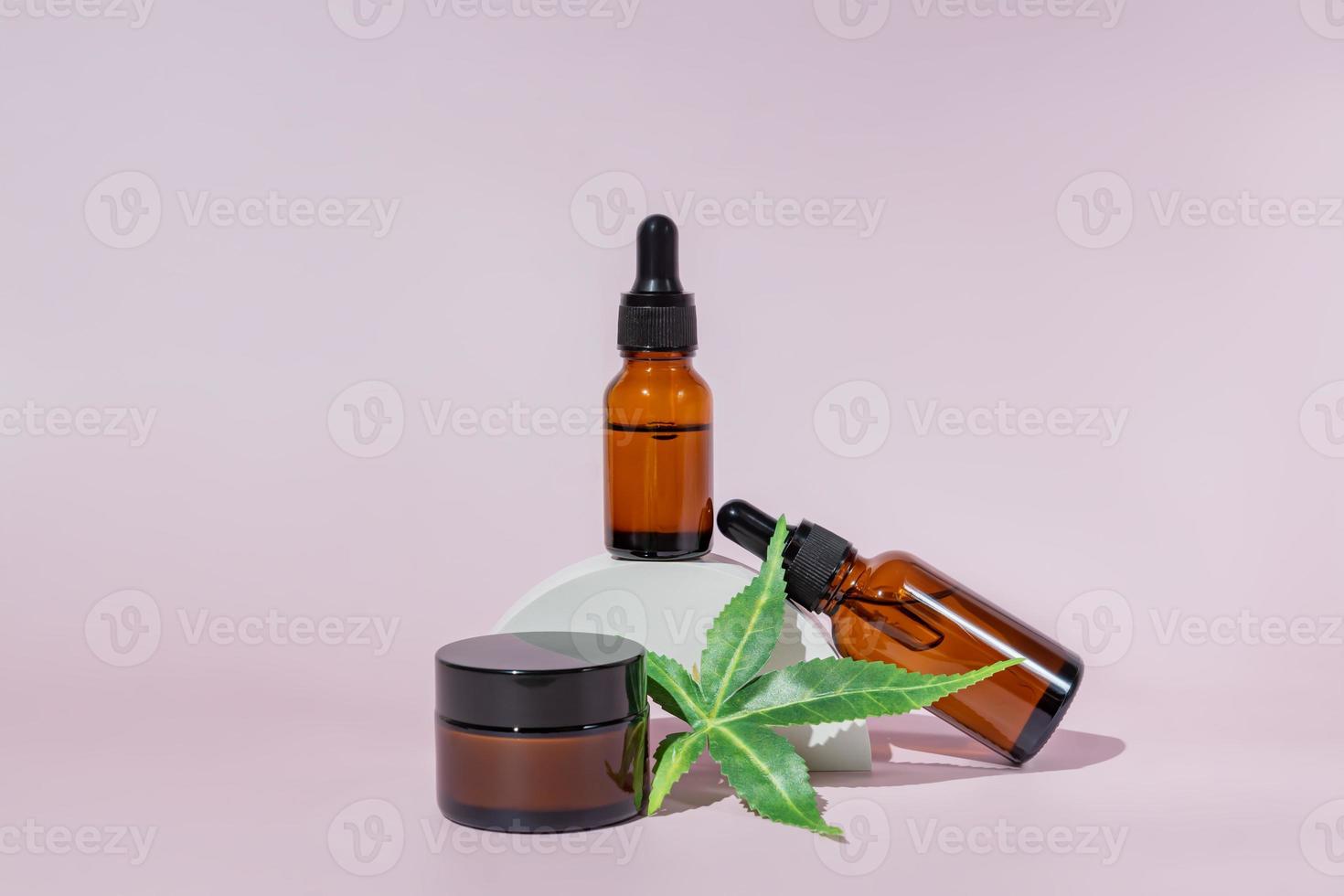 Alternative medicine, natural cosmetics. cbd oil, face cream in jar and cannabis leaves cosmetics on white concrete podium on pink background, copy space, mock up design photo