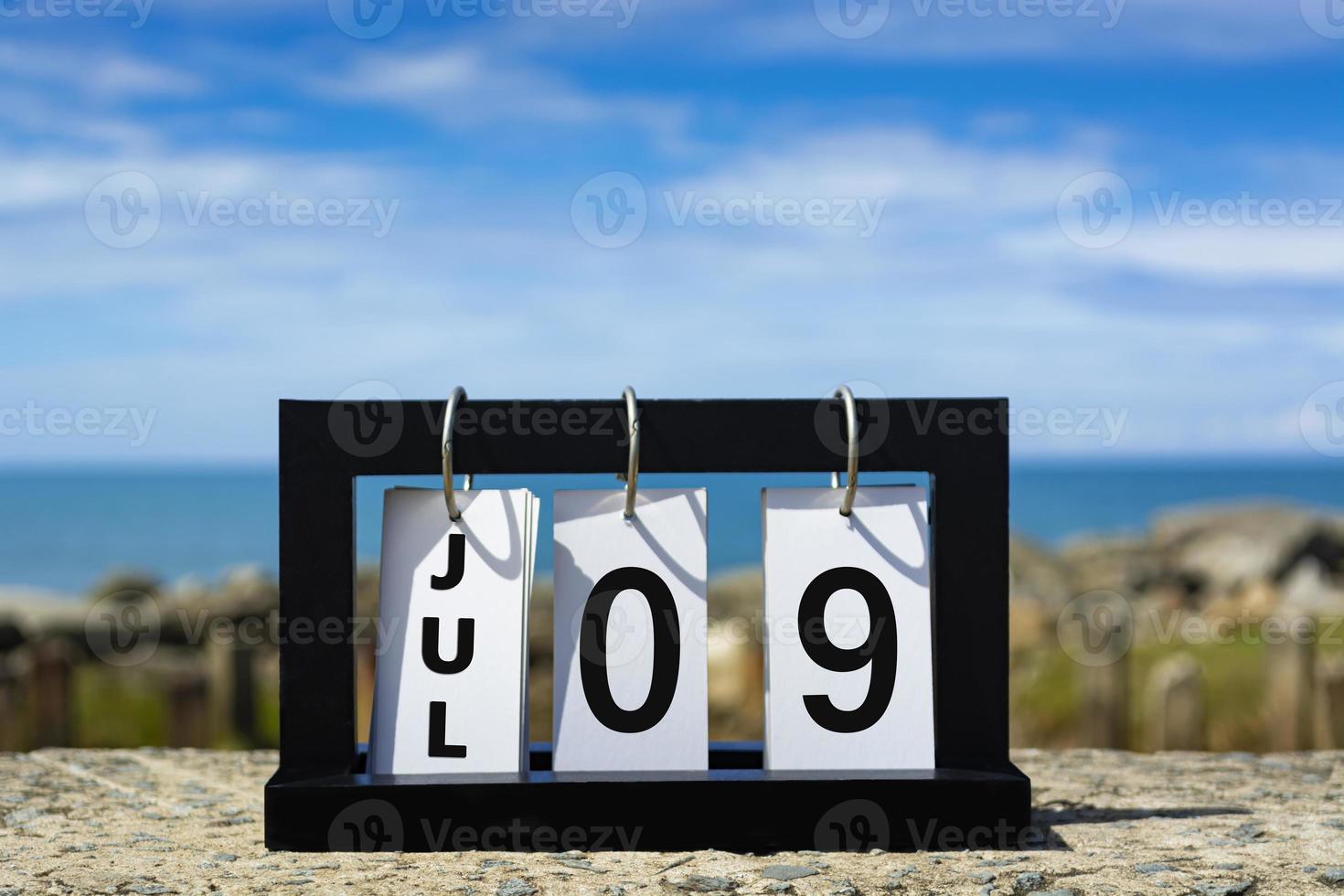 09 de julio texto de fecha de calendario en marco de madera con fondo borroso del océano. foto