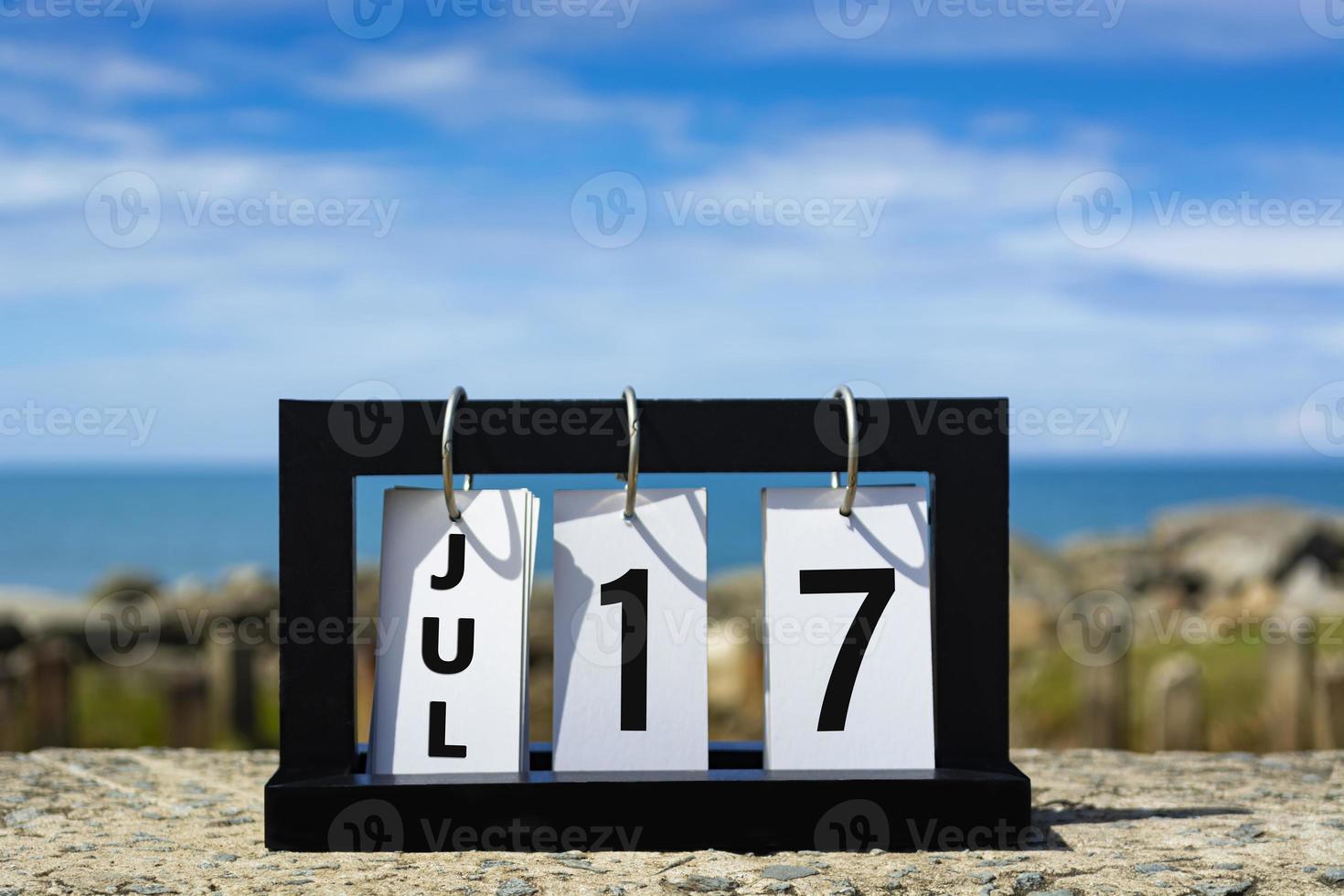 17 de julio texto de fecha de calendario en marco de madera con fondo borroso del océano. foto