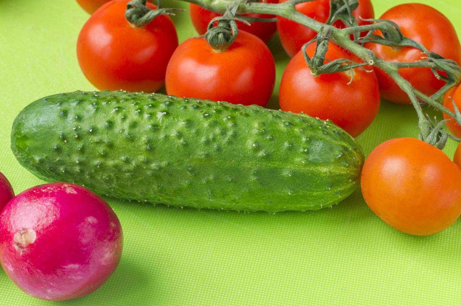 Red cherry tomatoes and green cucumbers on green cutting board photo