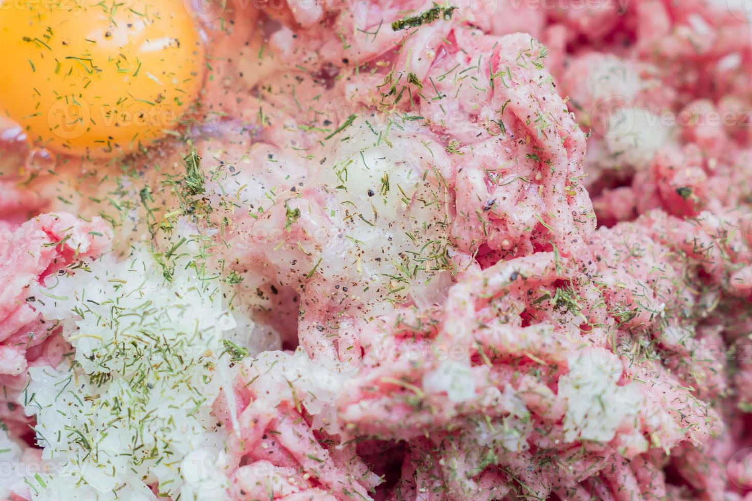 Minced meat in a bowl with raw egg, spices and chopped onion for cooking cutlets, selective focus photo